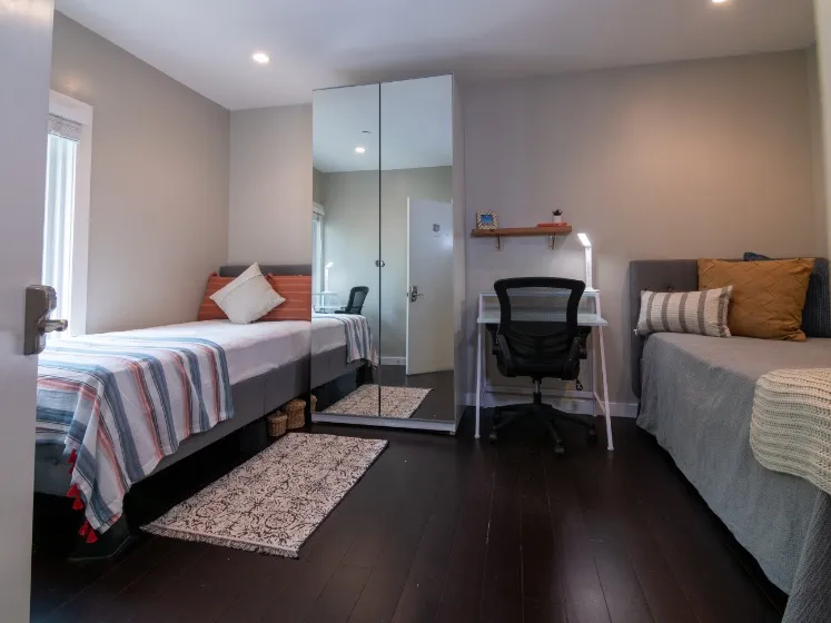 Cozy and modern bedroom featuring two single beds, a mirrored wardrobe, and a sleek study area with a comfortable desk chair.