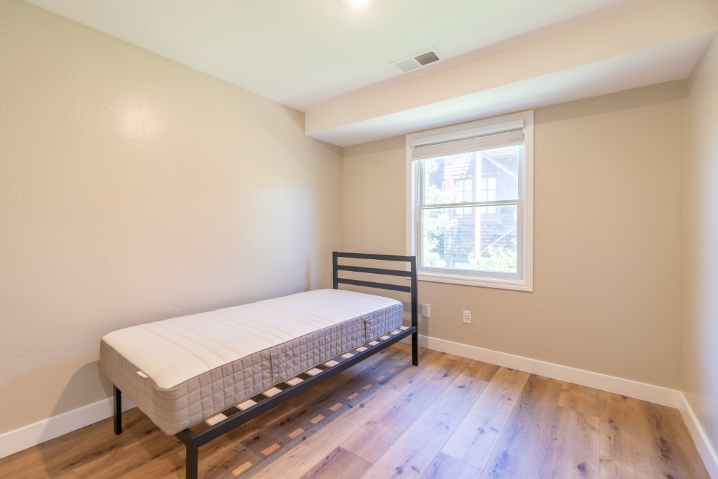 Bright and airy bedroom with modern bed frame, hardwood floors, and a large window offering natural light.