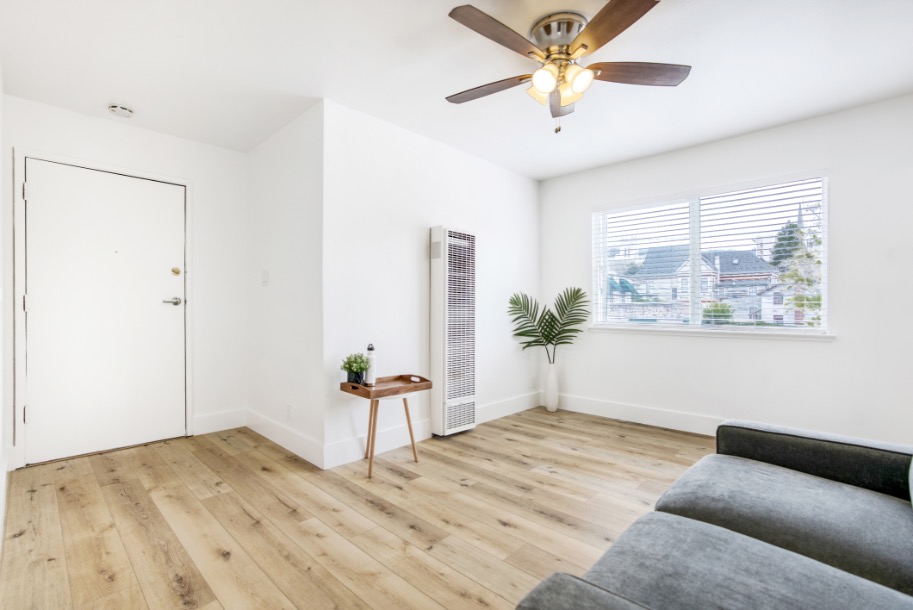 Bright and airy living room with large window, modern ceiling fan, and stylish wood flooring providing a cozy and inviting atmosphere.