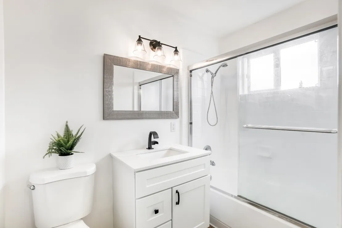 Bright and modern bathroom with sleek white vanity, large mirror, and a glass-enclosed shower, enhanced by elegant lighting.