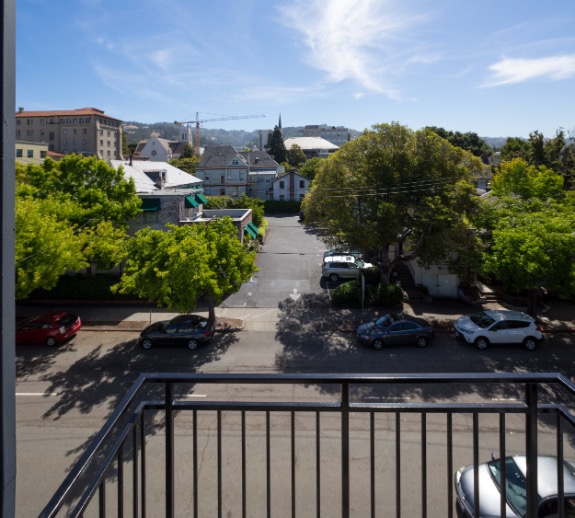 Charming balcony view overlooking a leafy street with quaint houses and bright, sunny skies.