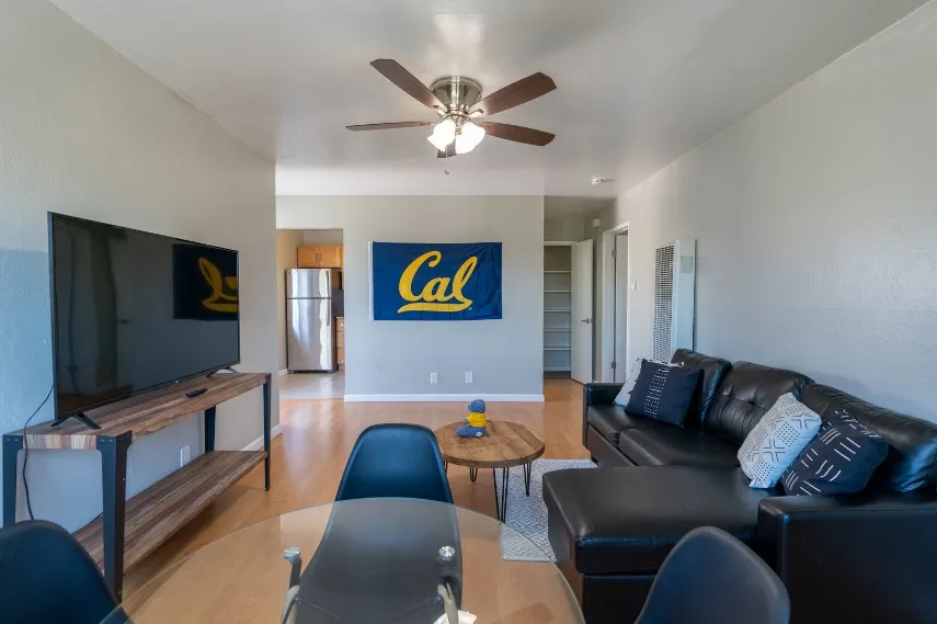 Inviting living room with modern decor, featuring a sleek black leather sofa, wall-mounted TV, and elegant ceiling fan for comfort.