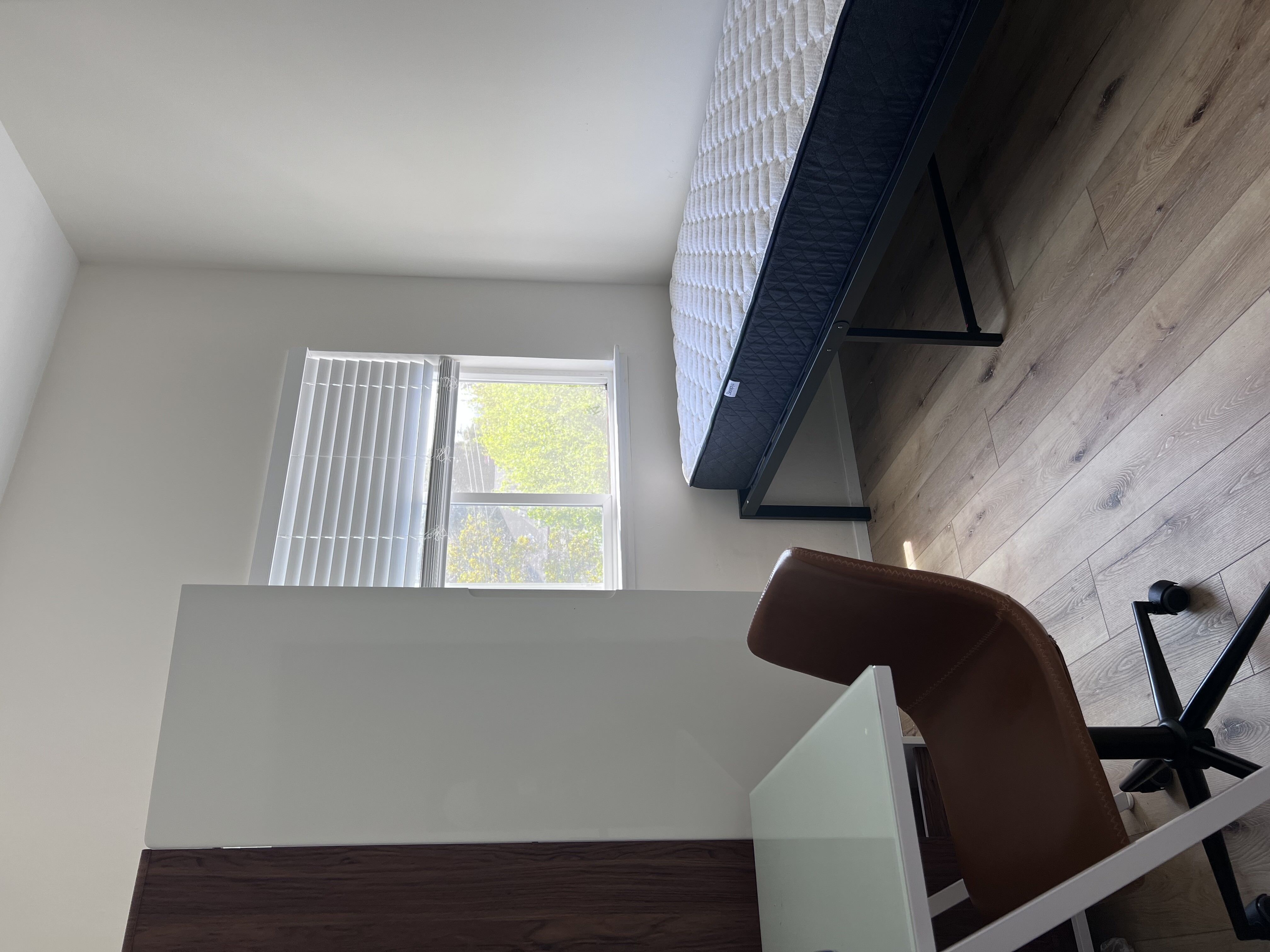 Bright and airy bedroom with modern furnishings, featuring a cozy bed, sleek desk, and stylish chair, bathed in natural light.