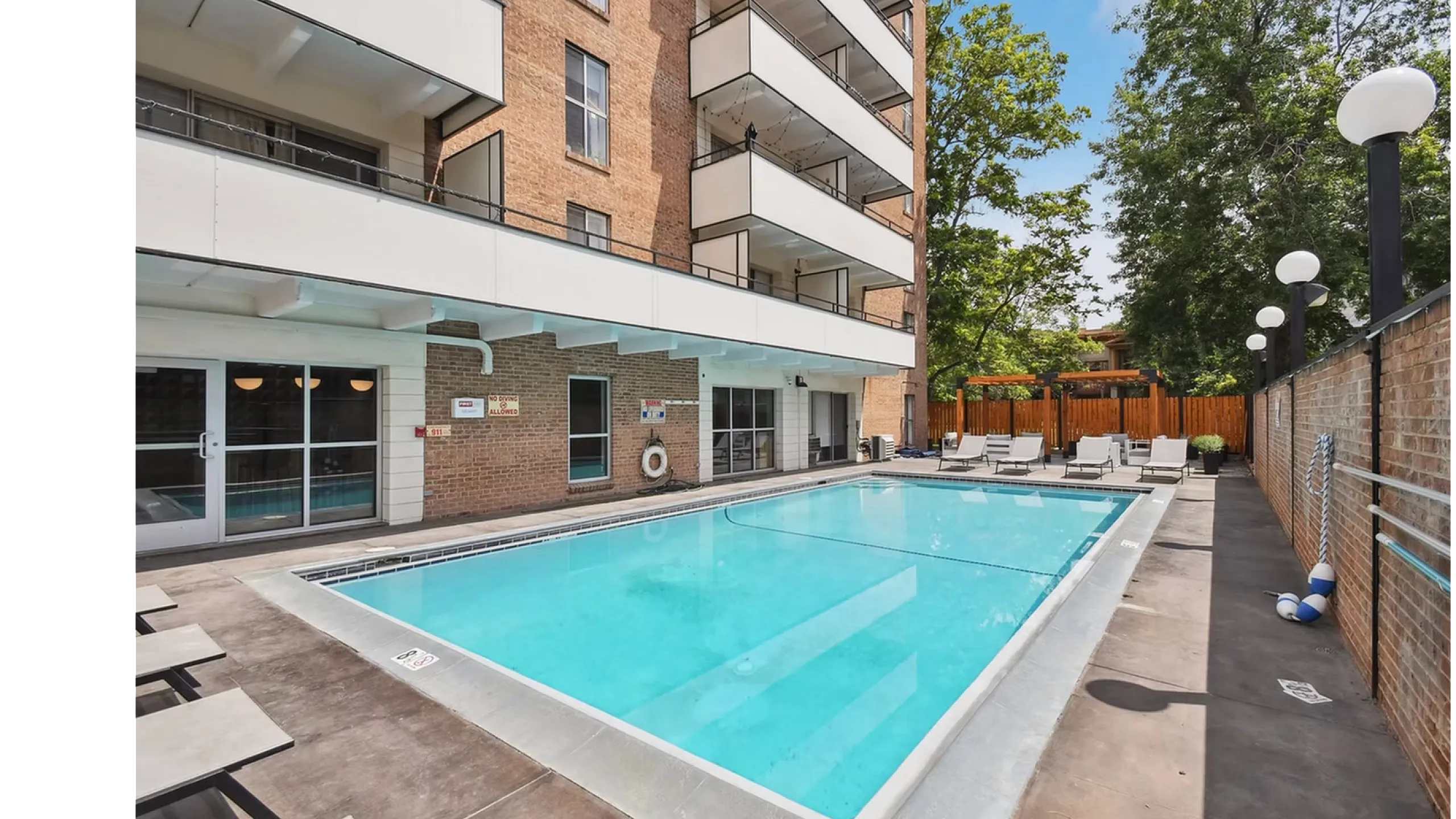 Inviting outdoor pool area with modern lounge chairs, surrounded by lush trees and a stylish apartment building, perfect for relaxation.
