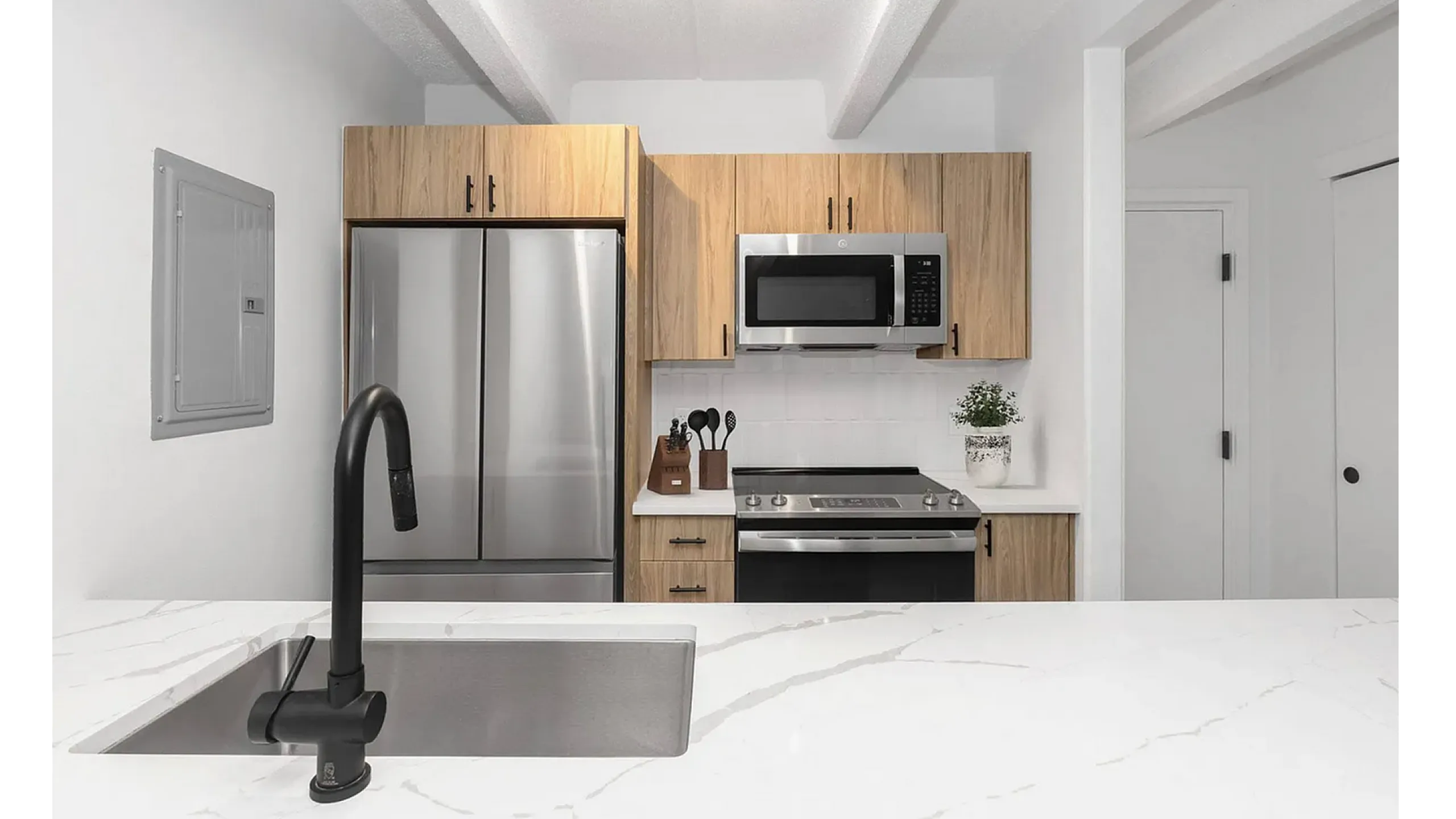 Modern kitchen with sleek stainless steel appliances, elegant wooden cabinetry, and stylish black fixtures against a pristine white countertop.
