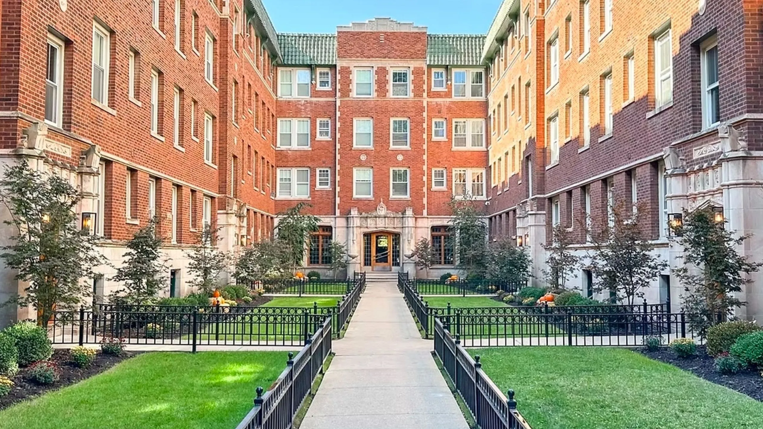 Charming brick apartment building with lush greenery and a welcoming pathway, offering urban living with a touch of elegance.
