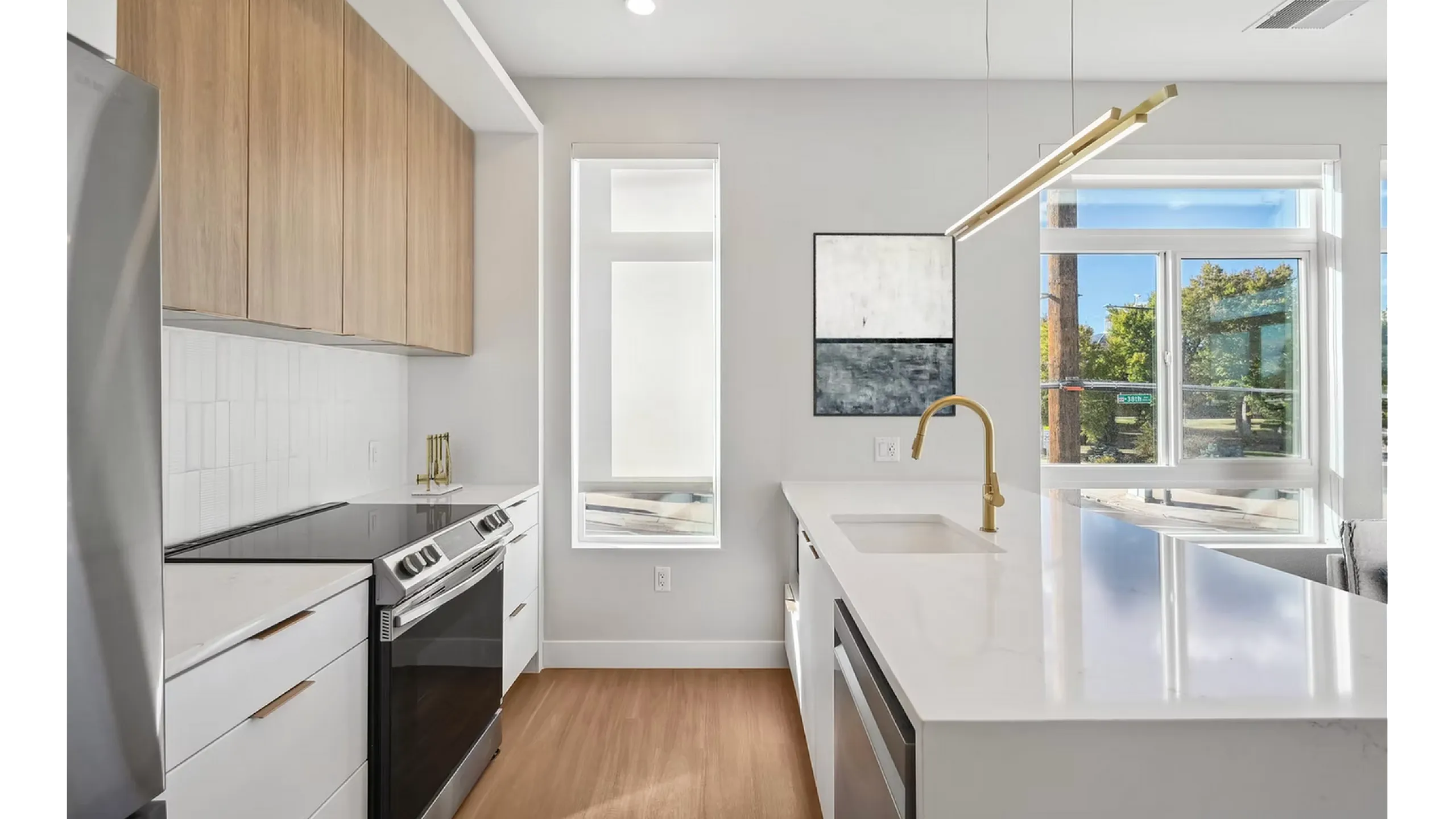 Modern kitchen featuring sleek cabinetry, quartz countertops, stainless steel appliances, and a chic gold faucet, flooded with natural light from large windows.