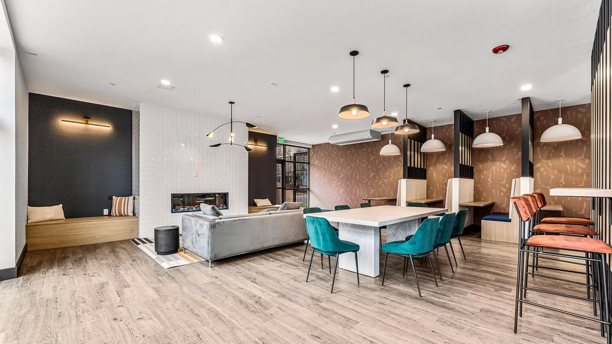 Modern communal lounge featuring elegant wooden flooring, a cozy fireplace, plush teal chairs, and stylish pendant lighting.