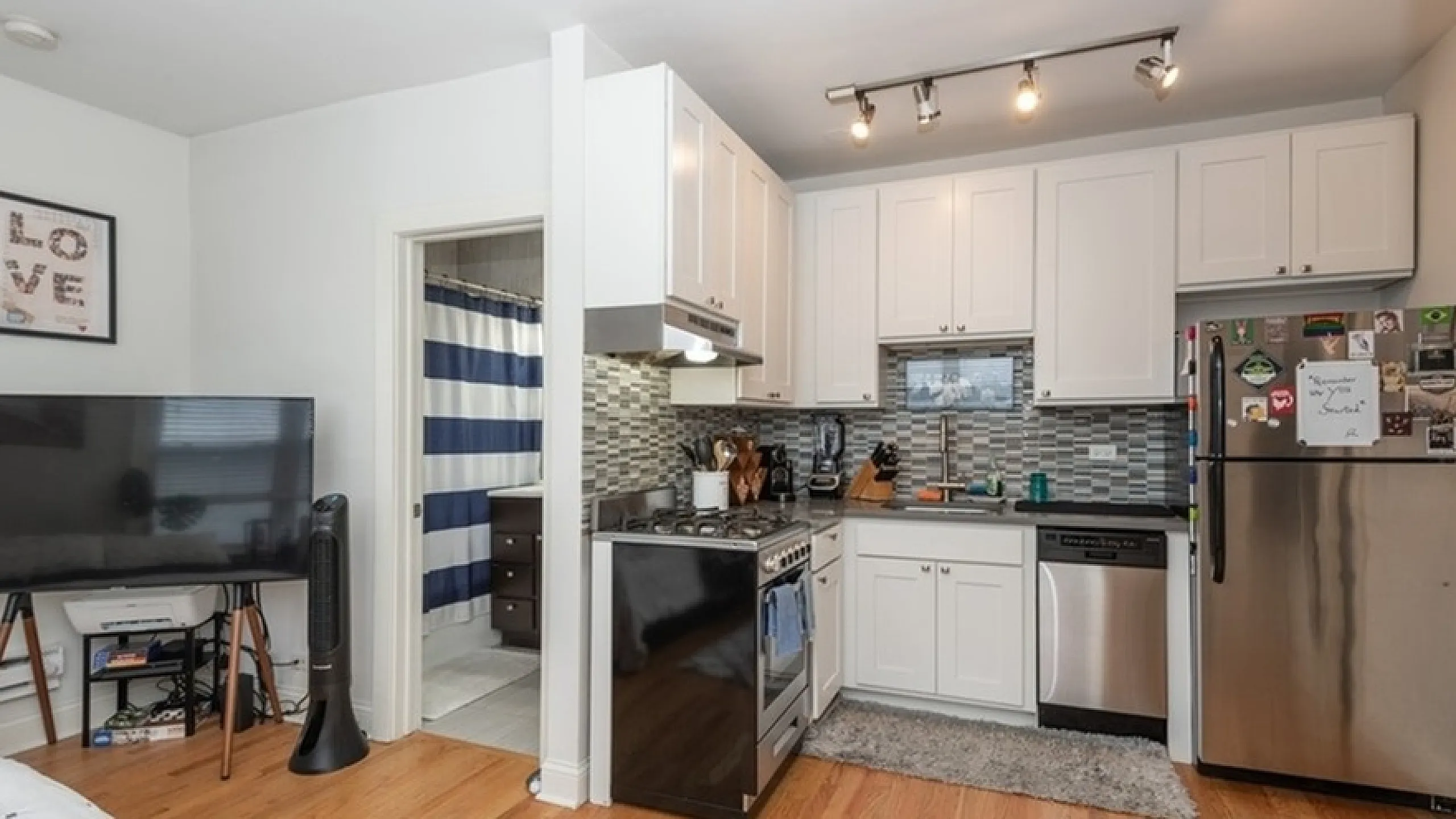 Contemporary kitchen with sleek stainless steel appliances, elegant white cabinetry, and cozy hardwood flooring, seamlessly blending into a bright living space.