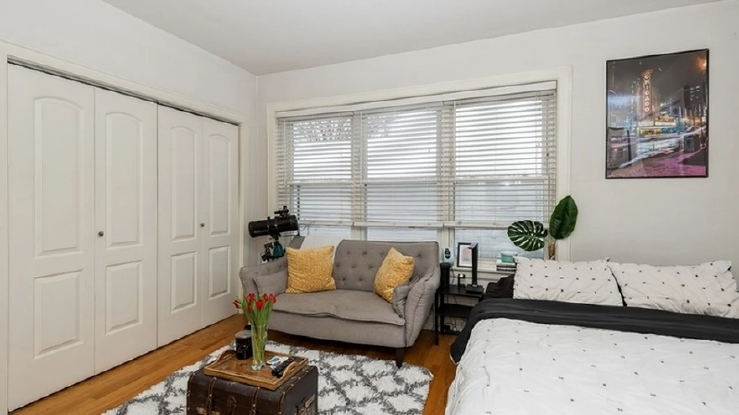 Bright and cozy bedroom featuring a stylish bed, elegant sofa, and rustic decor with natural light streaming through large windows.