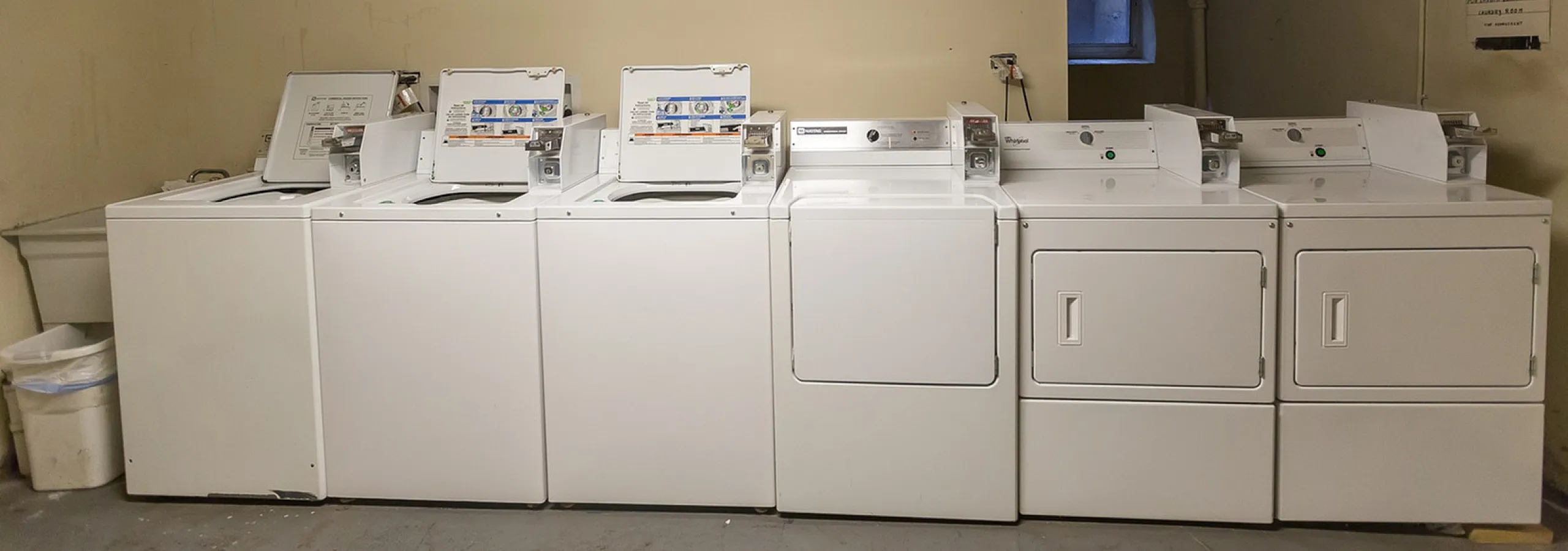 Bright and clean laundry room featuring multiple washing and drying machines, ideal for convenient apartment living.