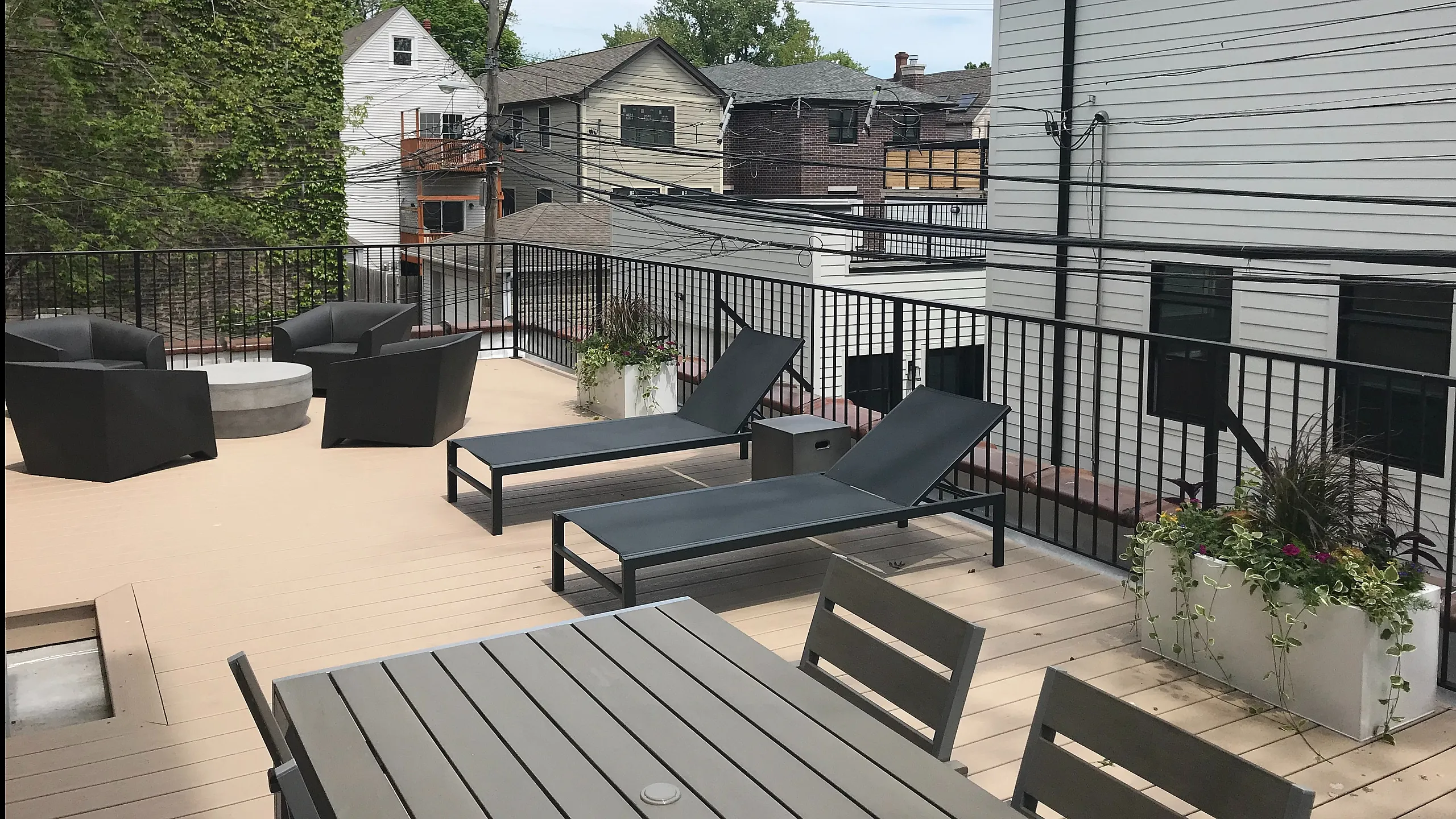 Chic outdoor terrace with modern seating, cozy fire pit, and lush planters offering an inviting space for relaxation and entertainment in a vibrant neighborhood setting.