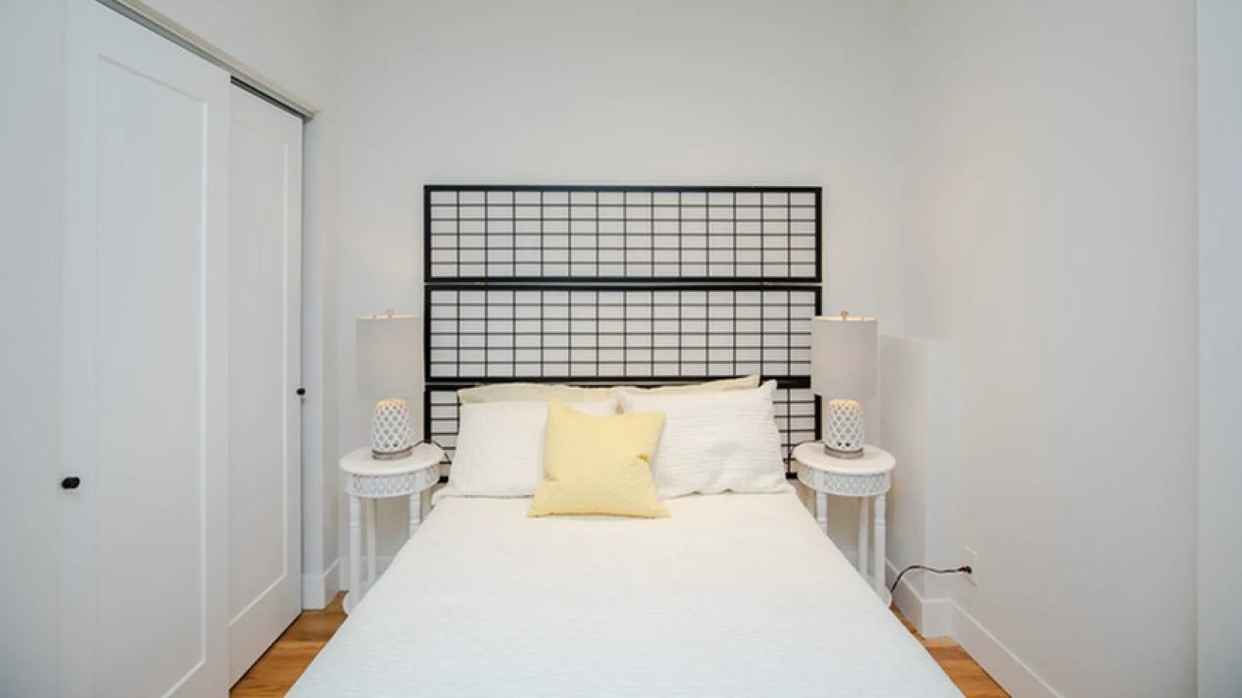 Charming bedroom with modern decor featuring a stylish bed, bright yellow accent pillow, and elegant bedside lamps.