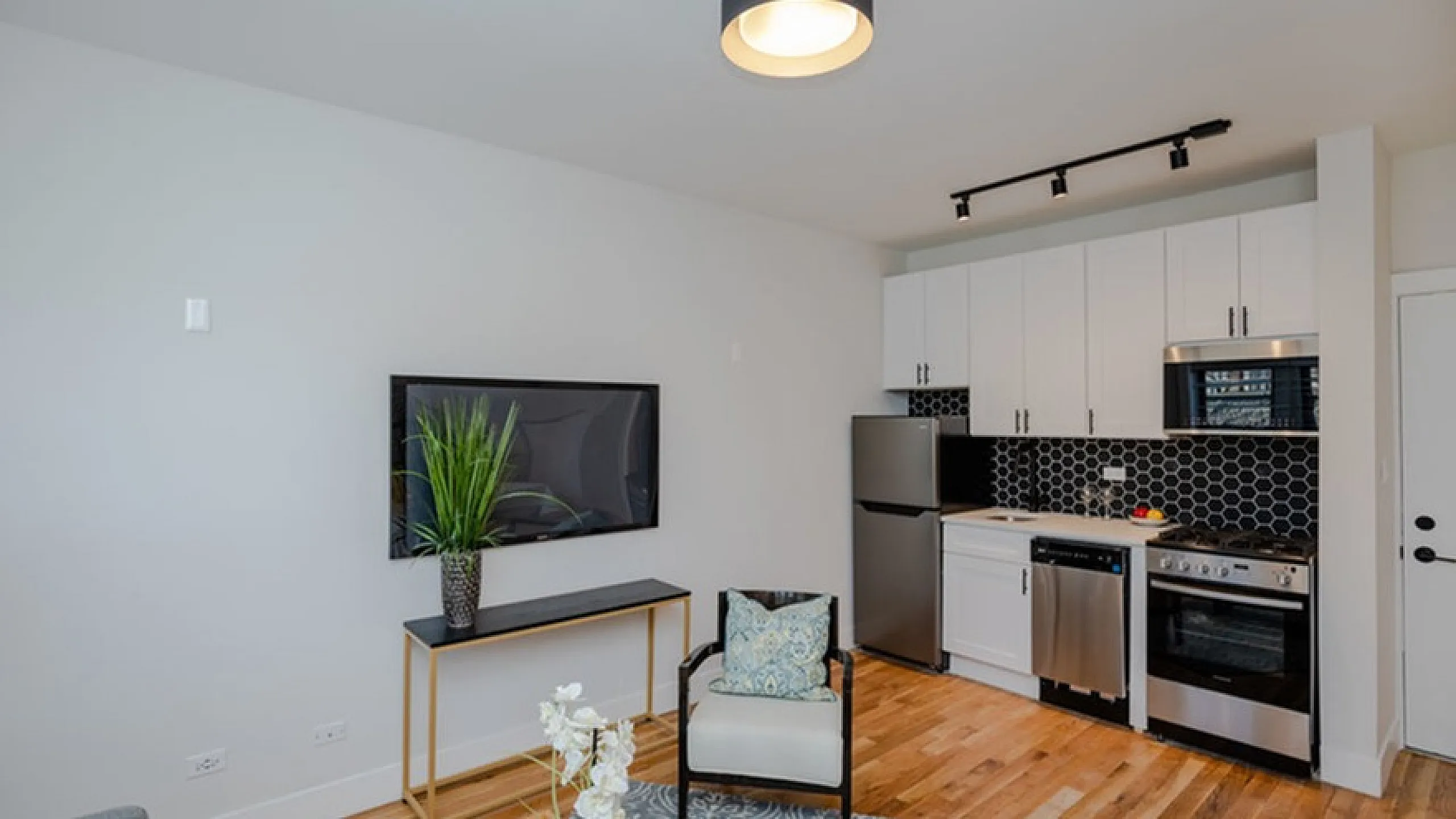 Modern open-concept living room and kitchen with sleek appliances, stylish furniture, and chic black hexagonal backsplash.