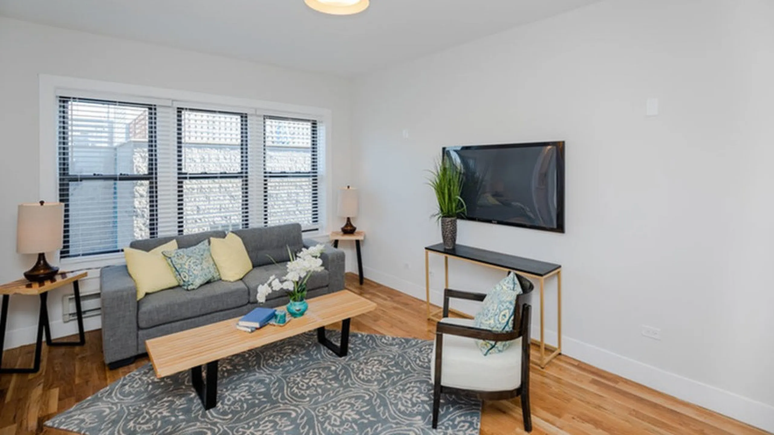 Bright and cozy living room featuring a modern gray sofa, stylish armchair, and elegant wooden floor, complemented by chic decor and a large window allowing natural light.