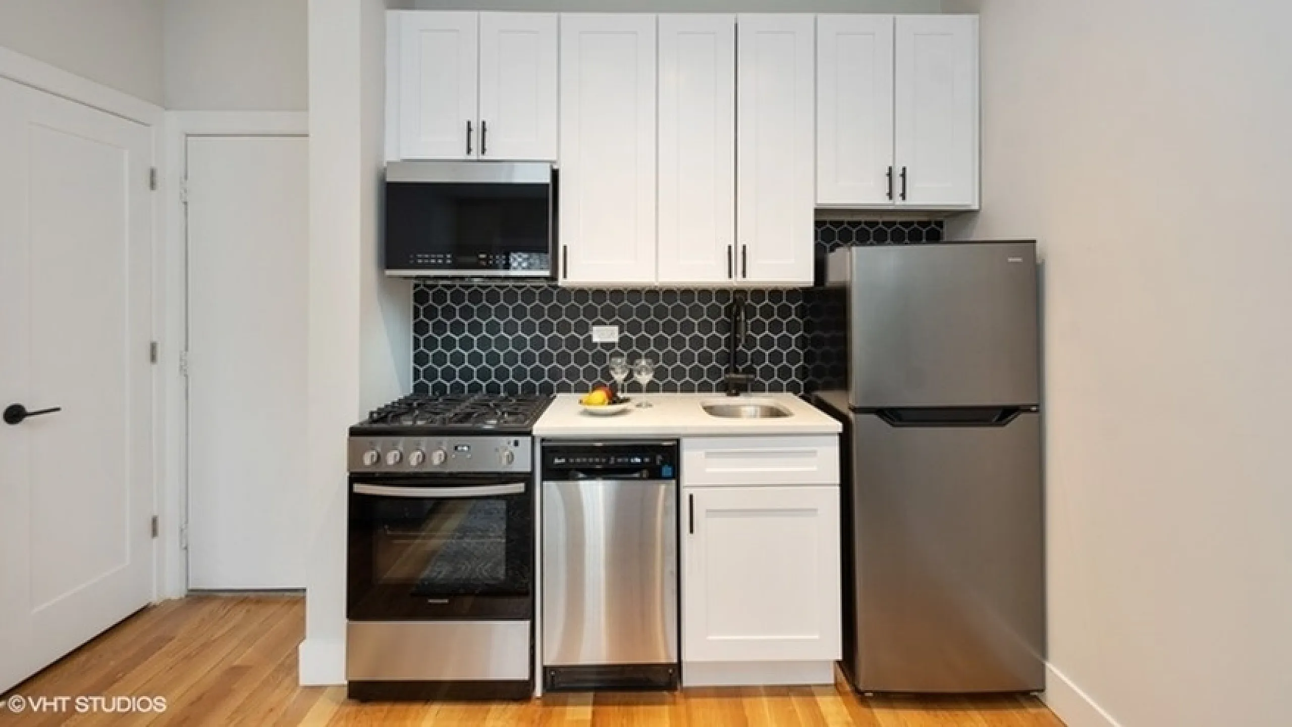 Chic and modern kitchen with sleek stainless steel appliances, glossy hexagonal backsplash, and ample white cabinetry.
