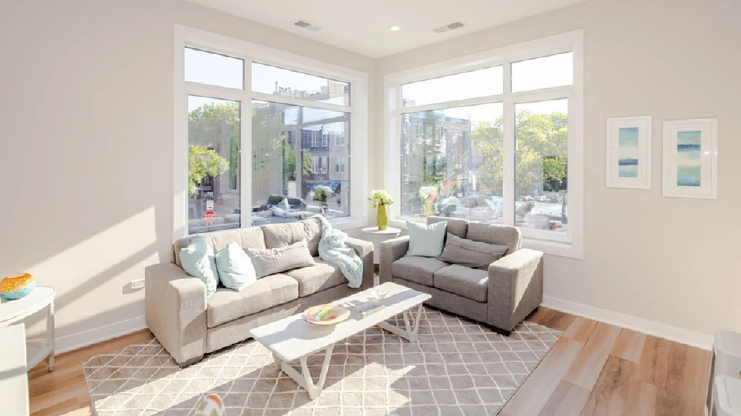 Bright living room with large windows, elegant grey sofas, and modern decor, offering a spacious and inviting atmosphere.