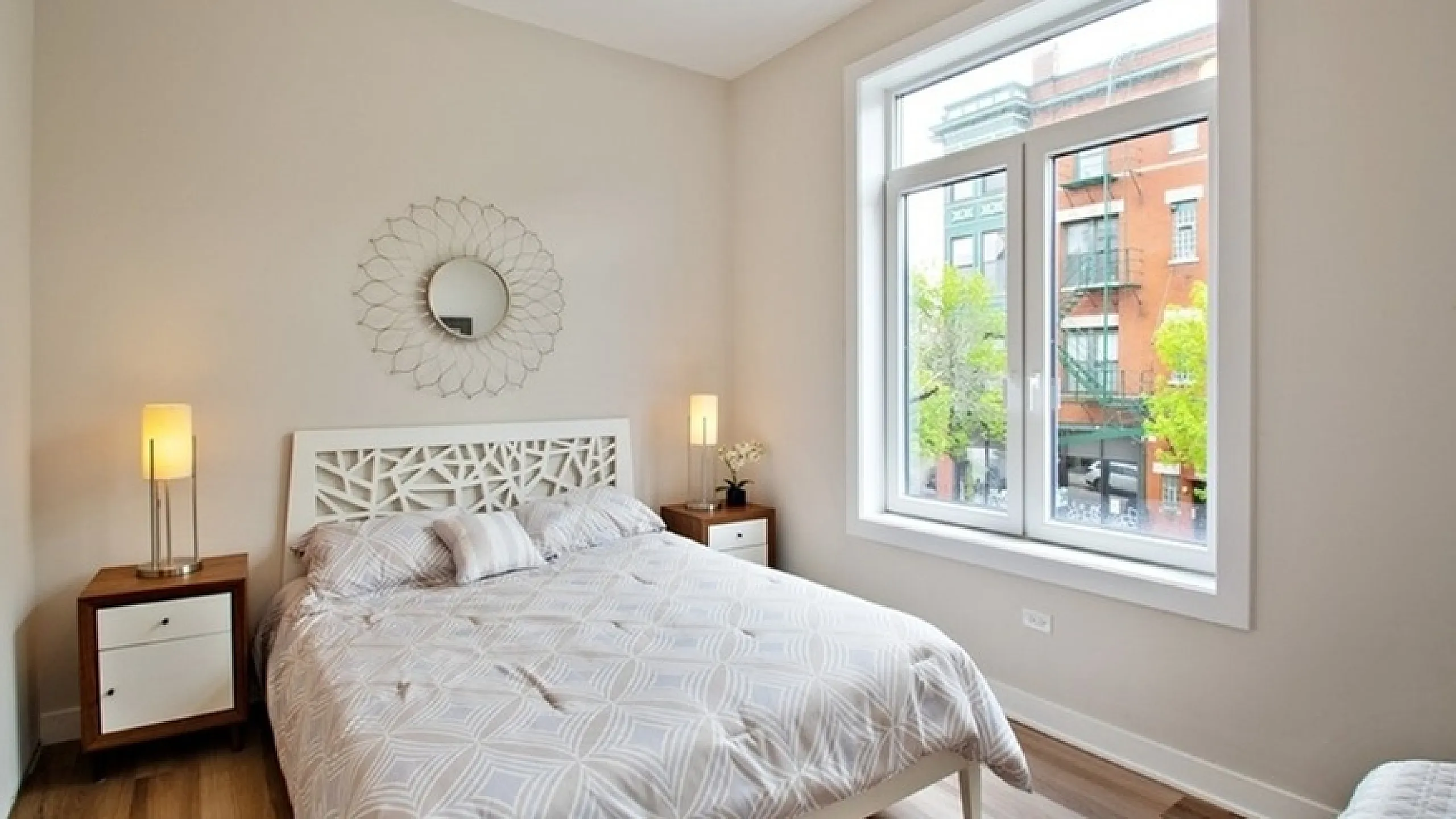 Bright and elegant bedroom with stylish decor, featuring a large window offering a charming city view.
