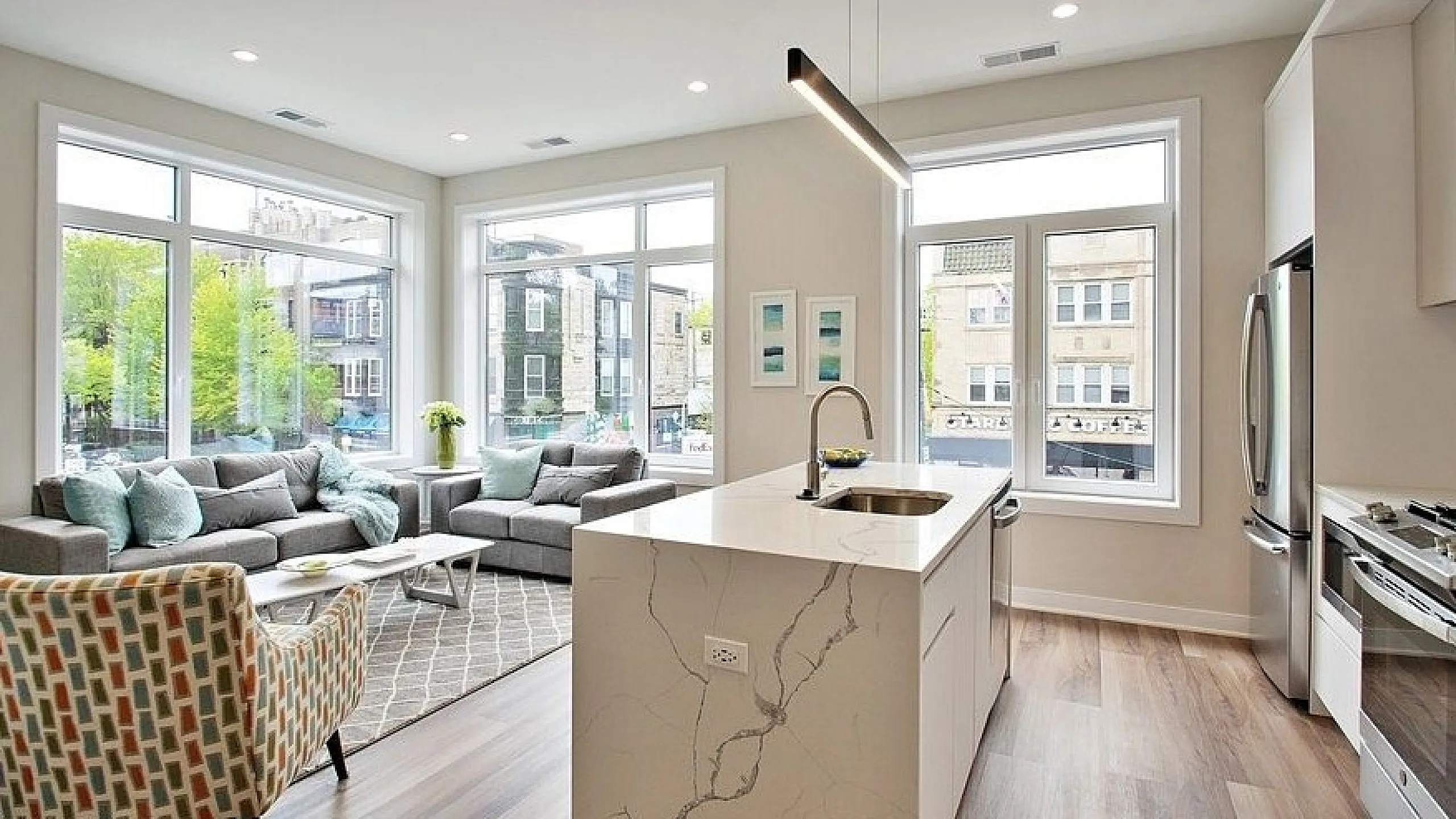 Bright and elegant open-concept living space featuring a modern kitchen with marble countertops and a cozy seating area with large windows.