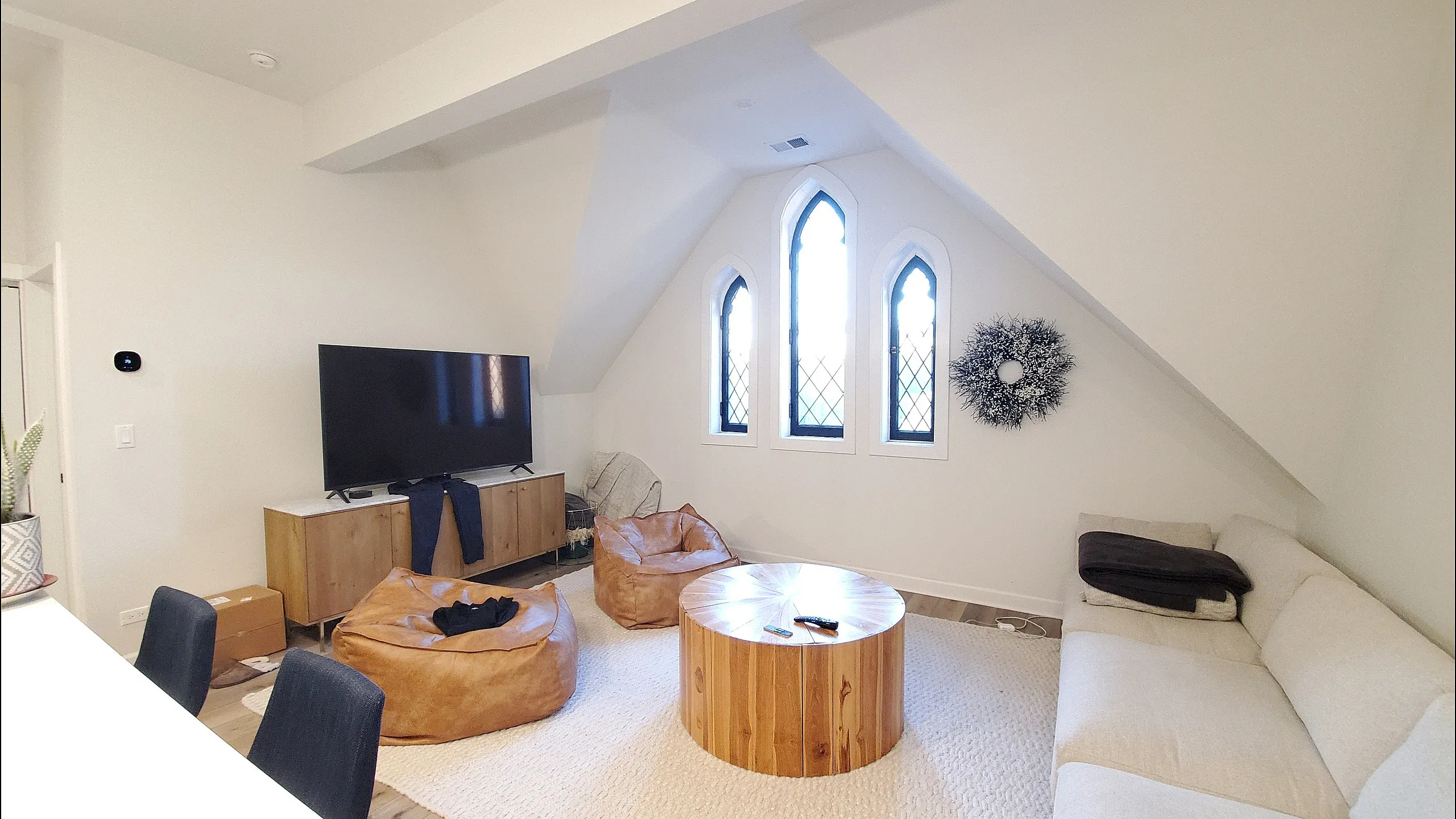 Charming living space featuring a cozy couch, stylish wooden accents, and a large TV under elegant arched windows.