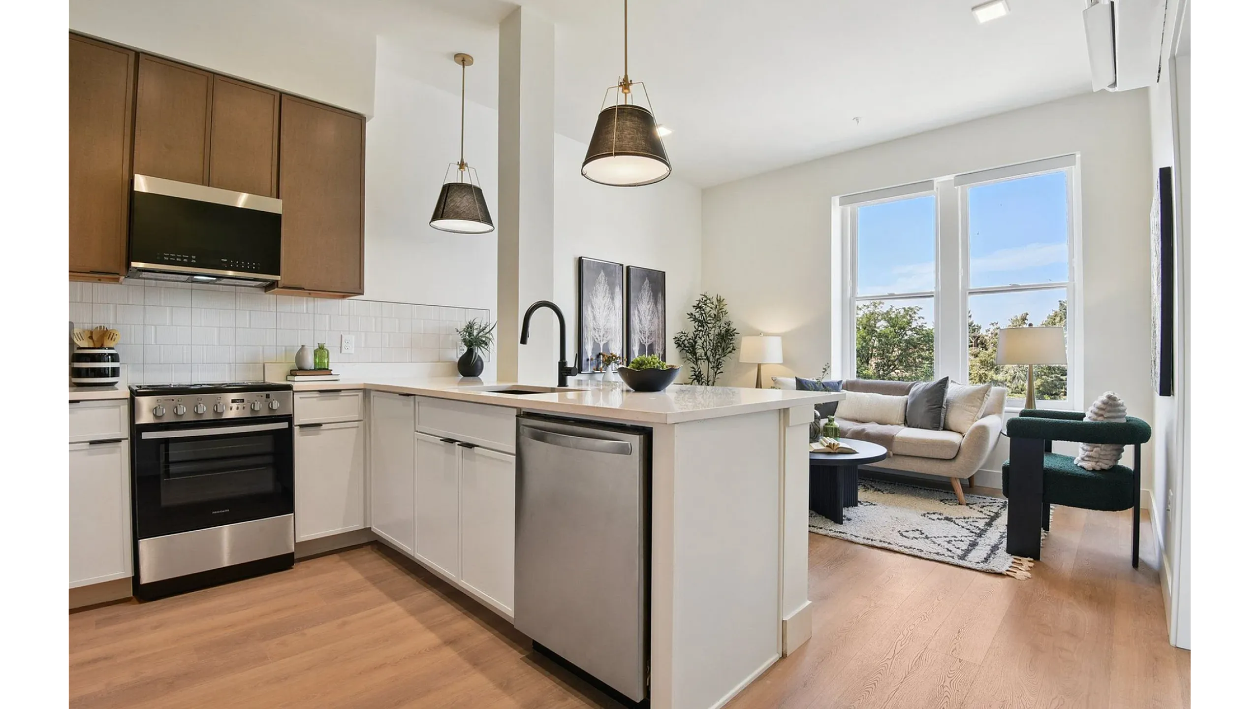 Bright, modern open-concept kitchen with sleek appliances, wooden cabinetry, and cozy living area with large windows and stylish decor.