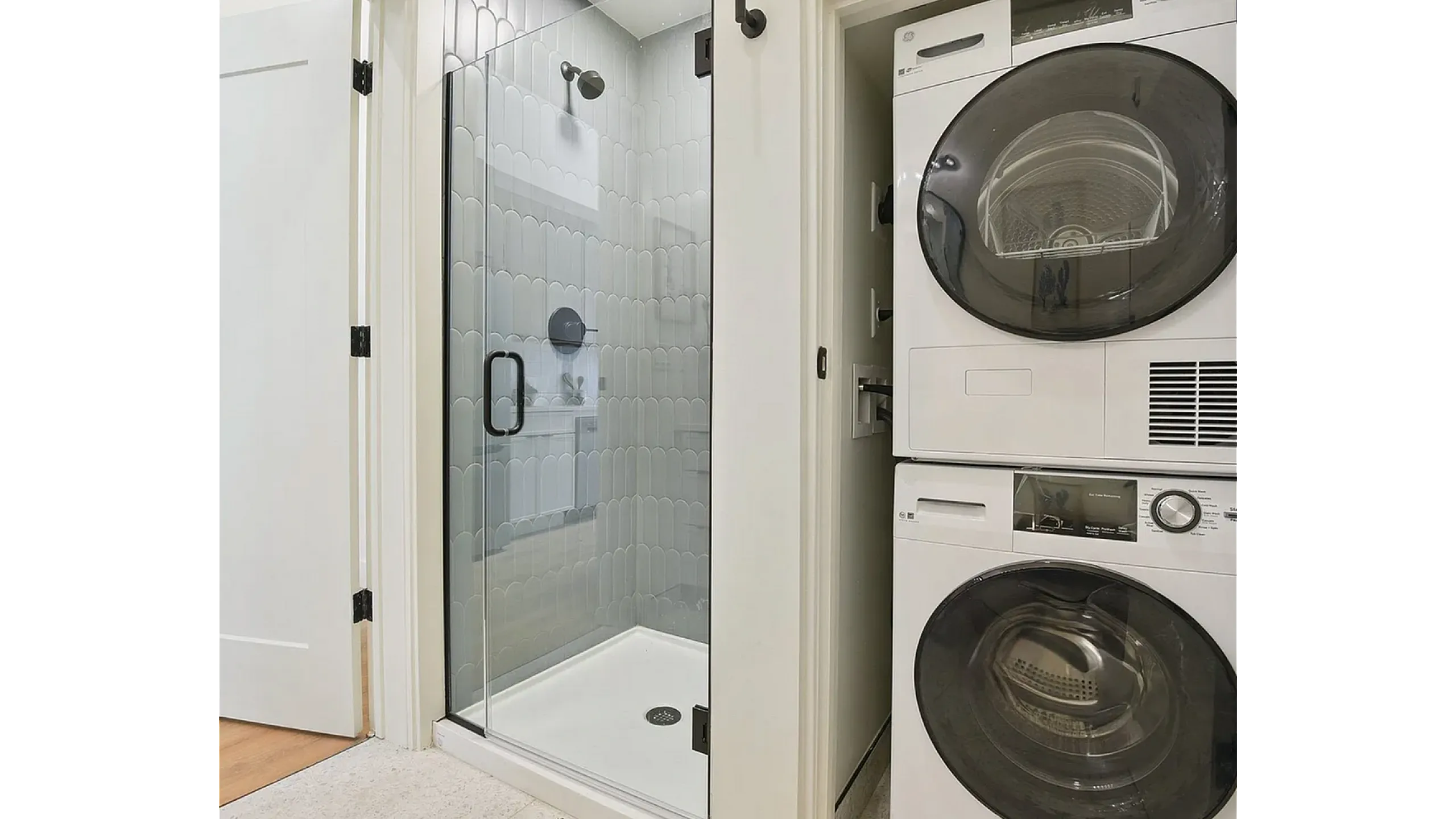 Contemporary bathroom with elegant glass shower and stackable washer-dryer, featuring chic tile design and efficient use of space.