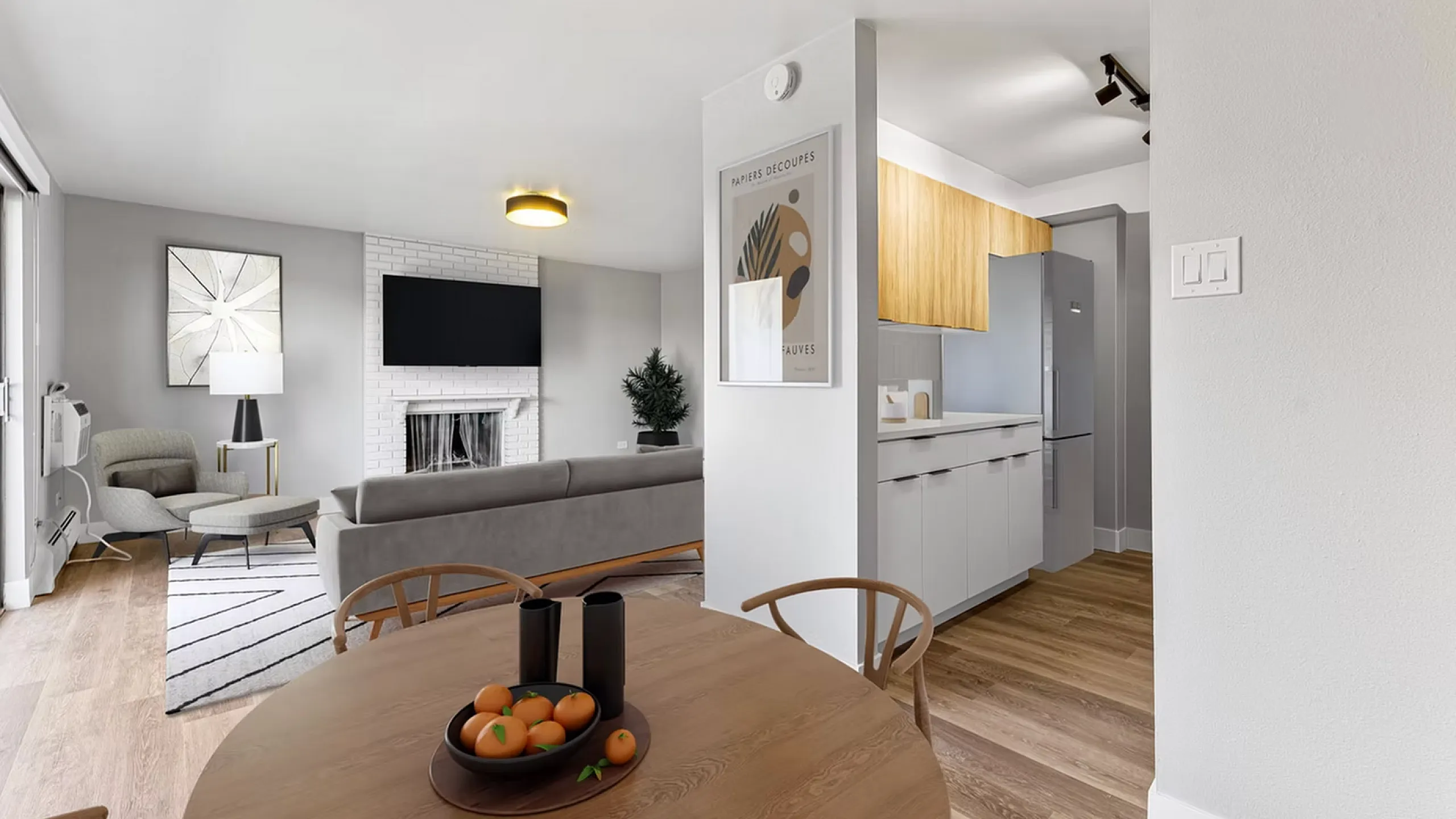 Modern living space with cozy seating area, stylish fireplace, and sleek kitchen. Bright ambiance with wood flooring and contemporary decor.