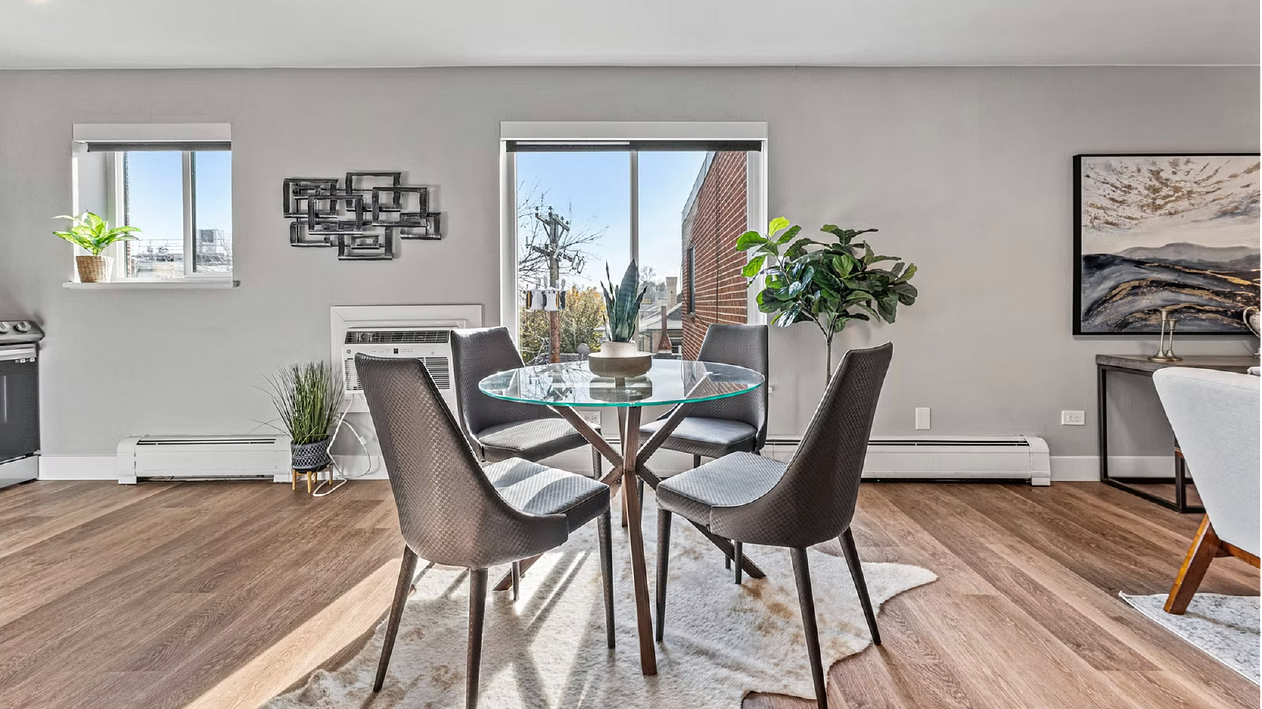 Bright and modern dining area with a glass table and stylish chairs, complemented by sunlight streaming through large windows and lush greenery, offering a welcoming ambiance.