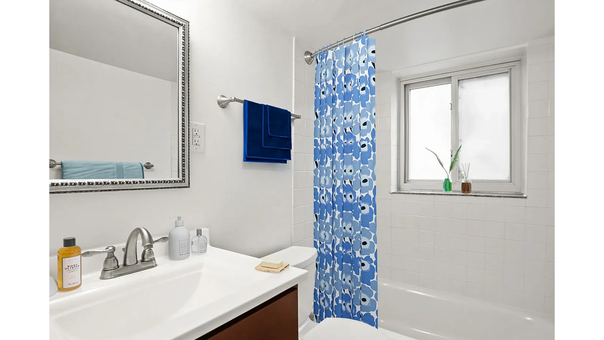 Bright modern bathroom with stylish blue floral shower curtain, elegant vanity, and cozy window view.