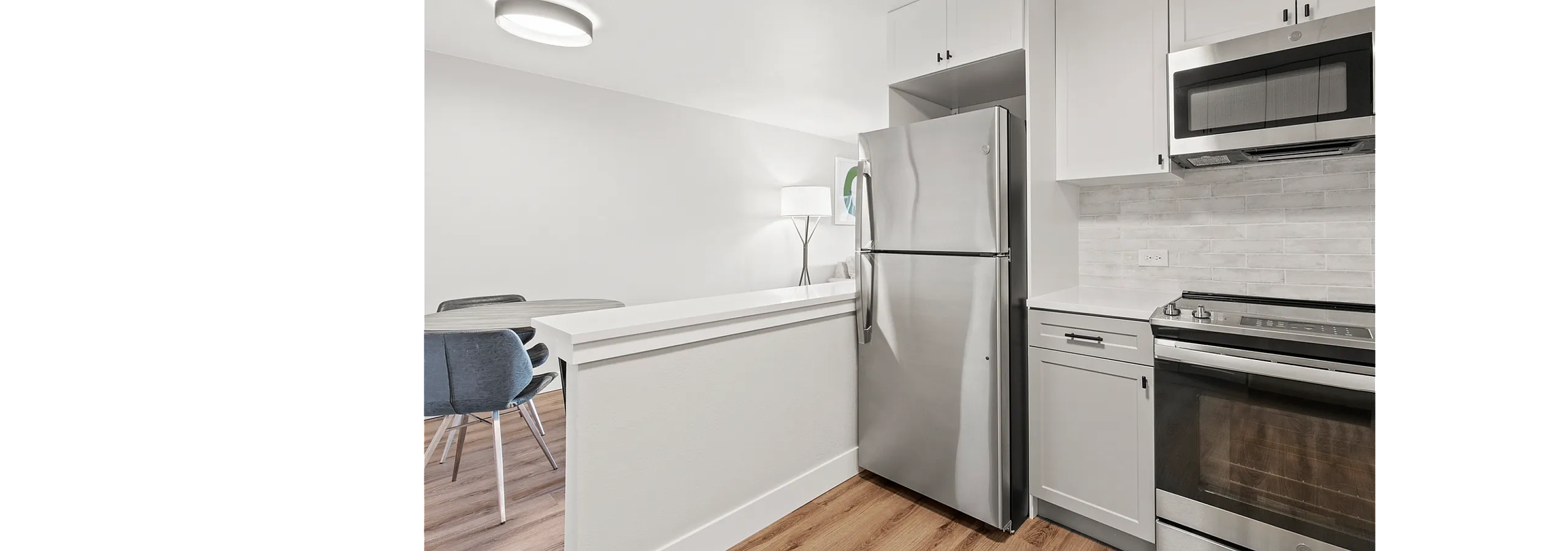 Modern kitchen with sleek stainless steel appliances, white cabinetry, and elegant wood flooring, opening into a cozy dining area with stylish seating.