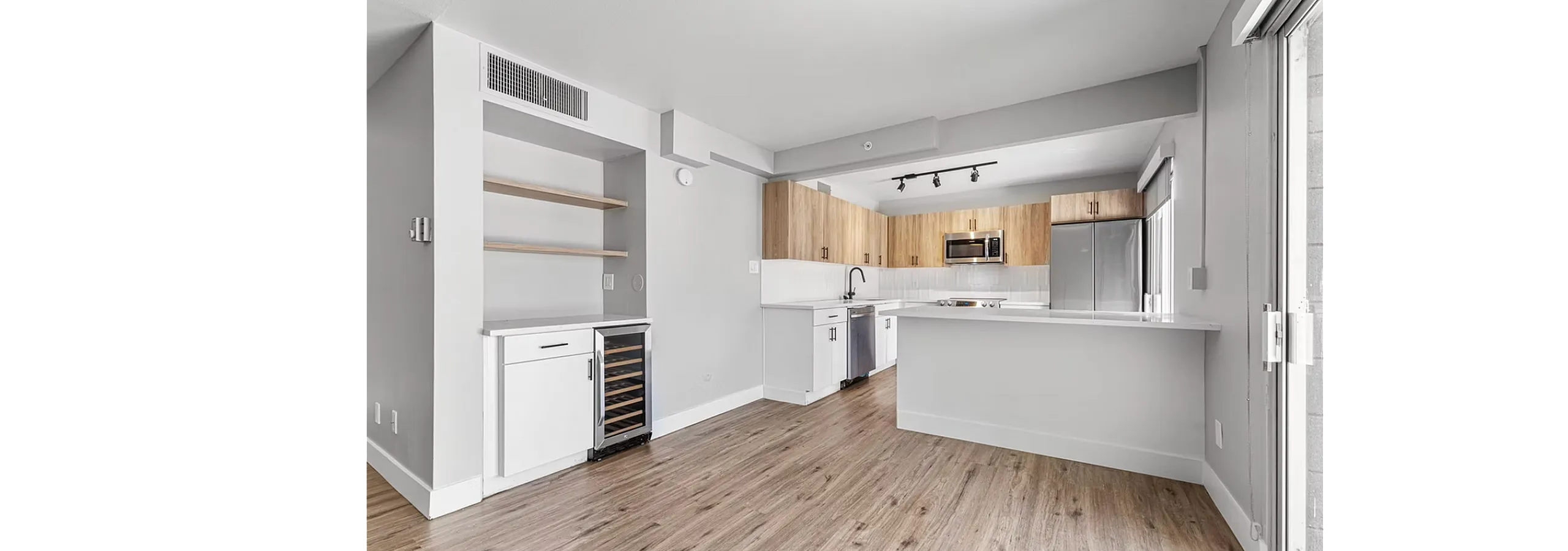 Modern open-concept kitchen with sleek wood floors, stainless steel appliances, and ample natural light through large windows.