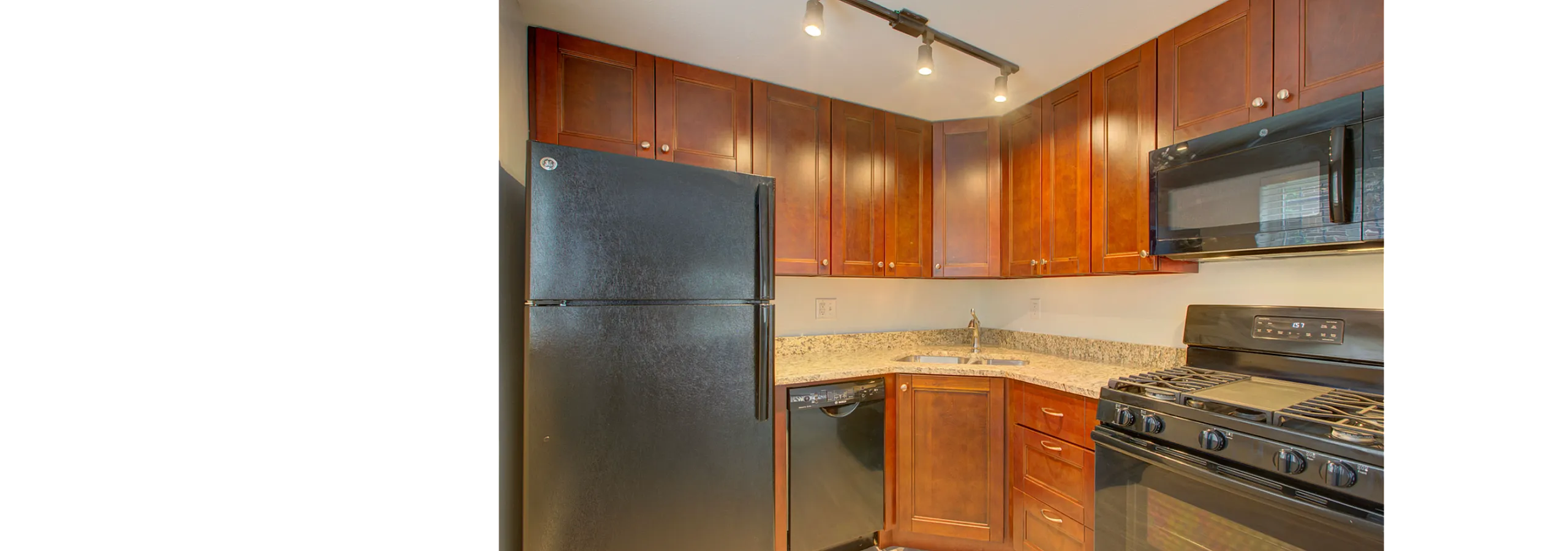 Charming kitchen featuring rich wooden cabinets, sleek black appliances, and elegant granite countertops, illuminated by modern track lighting.
