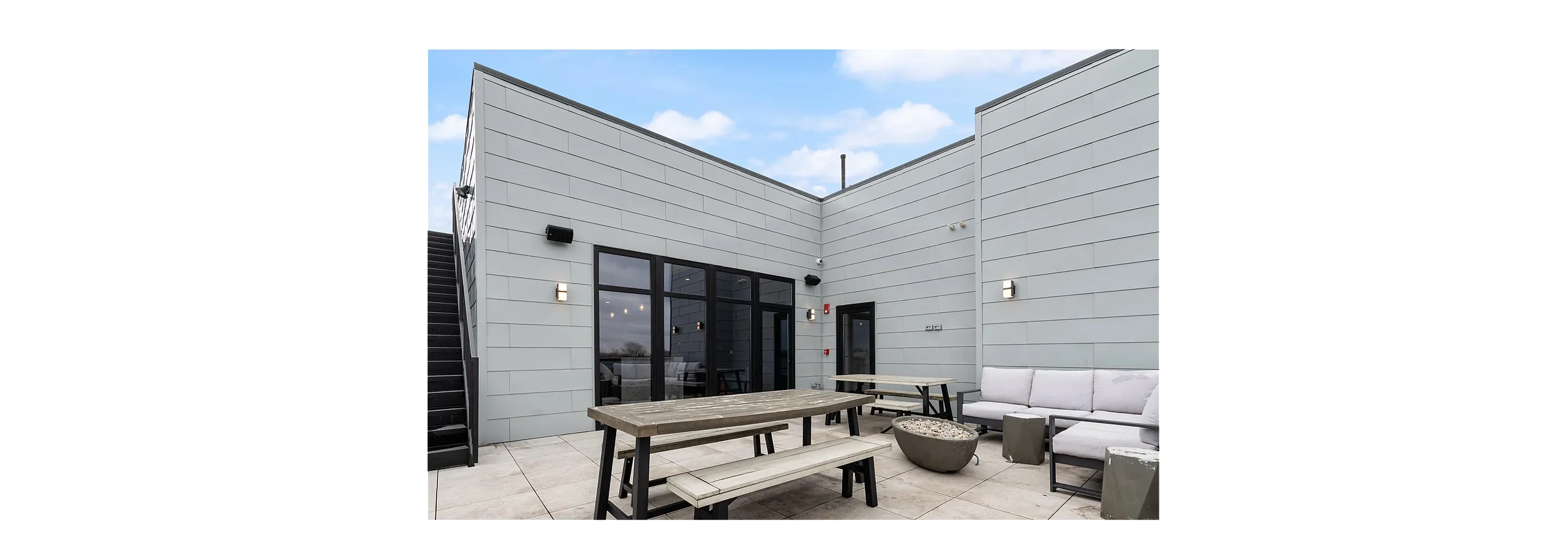 Chic outdoor terrace featuring modern seating, stylish picnic tables, and sleek architectural design under a clear blue sky.