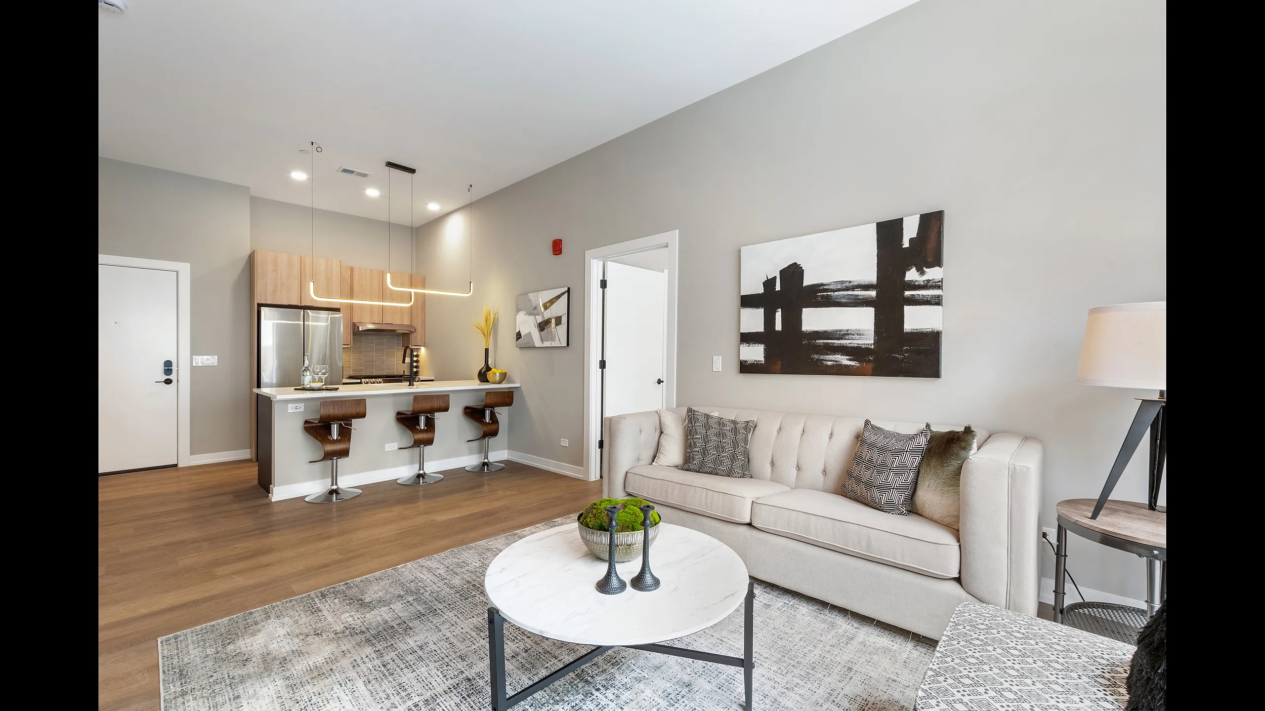 Contemporary open-concept living space with chic decor, featuring a plush sofa, sleek kitchen with modern bar stools, and stylish artwork.