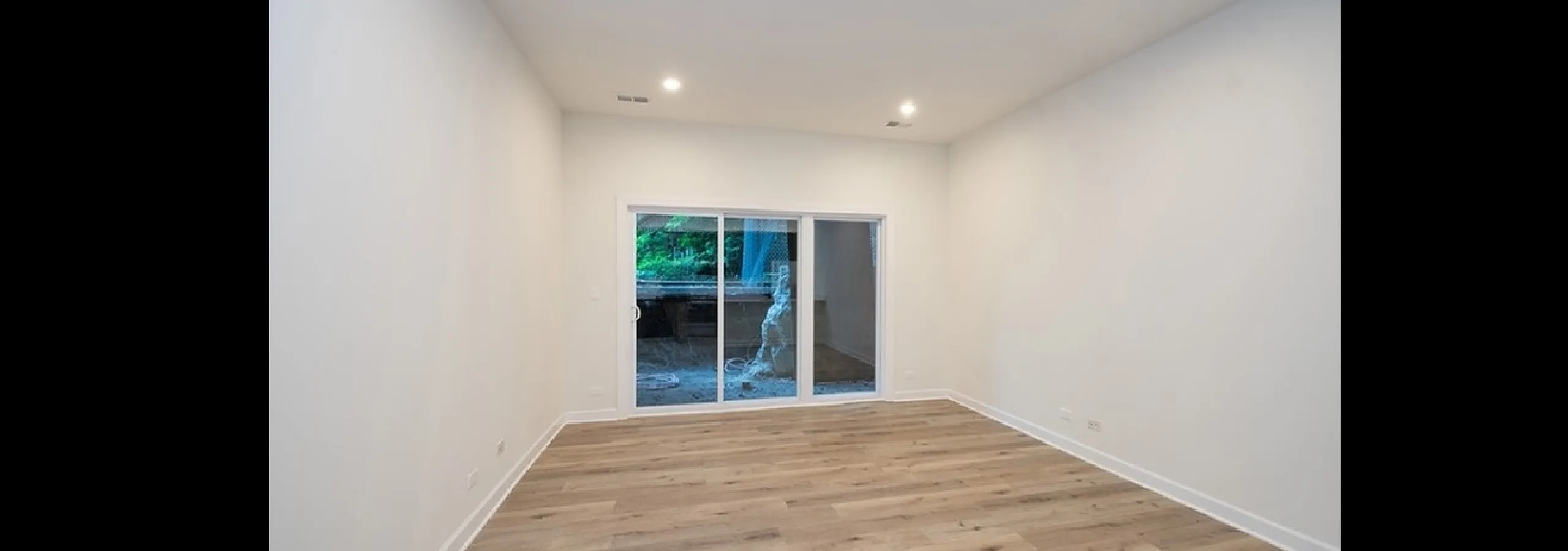 Sleek apartment room with elegant wood flooring, recessed lighting, and a large sliding glass door offering scenic outdoor views.