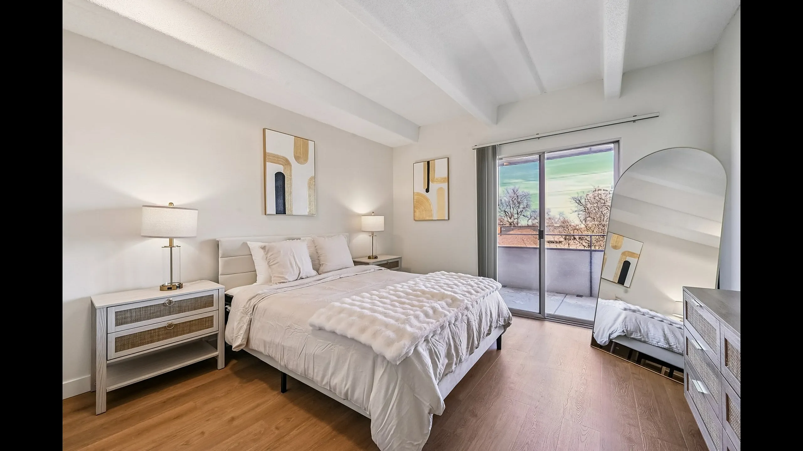 Bright and inviting bedroom with plush bedding, modern artwork, and sliding glass doors leading to a scenic balcony view.