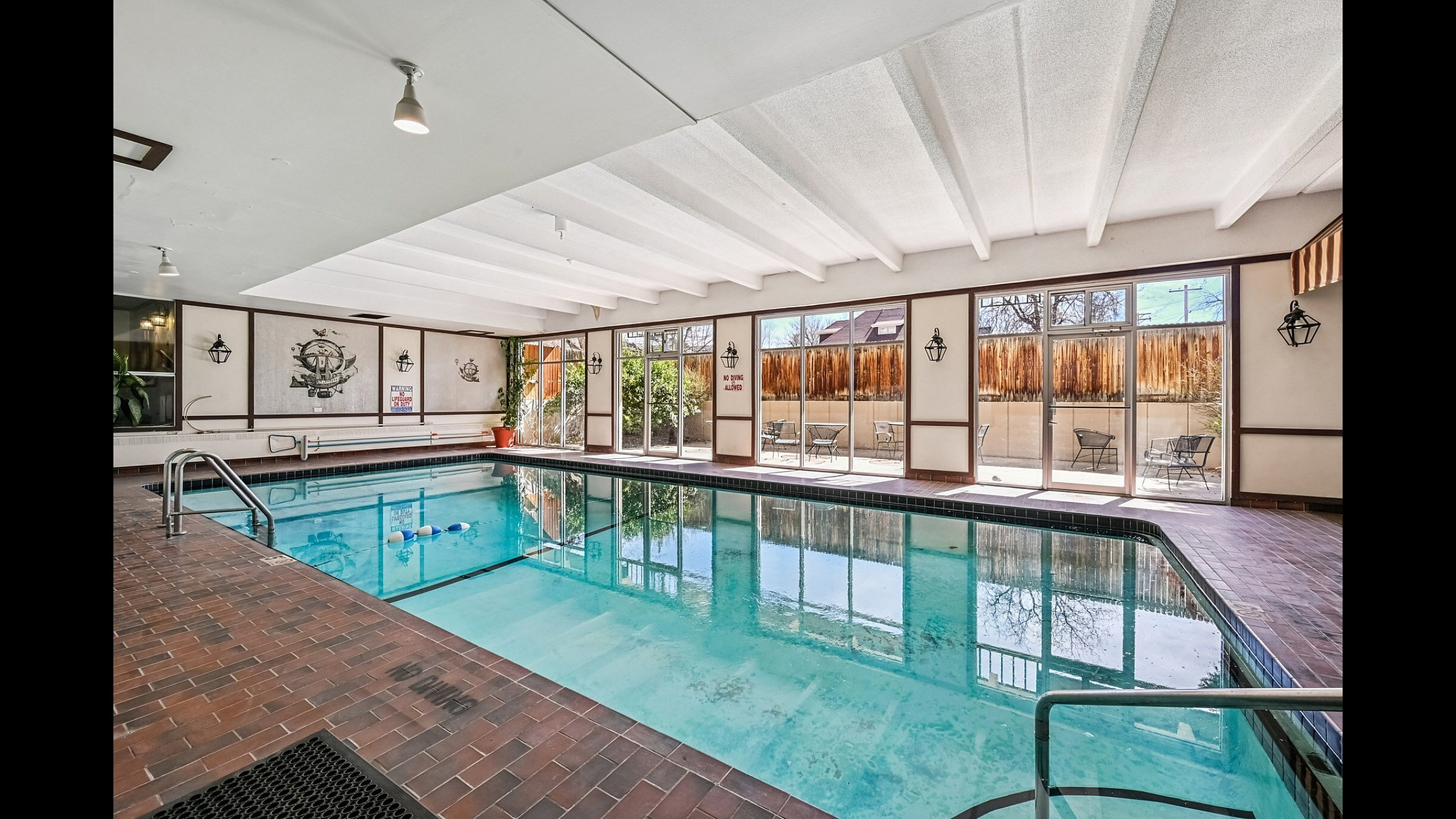 Luxurious indoor swimming pool with stylish brick flooring and large windows offering abundant natural light.