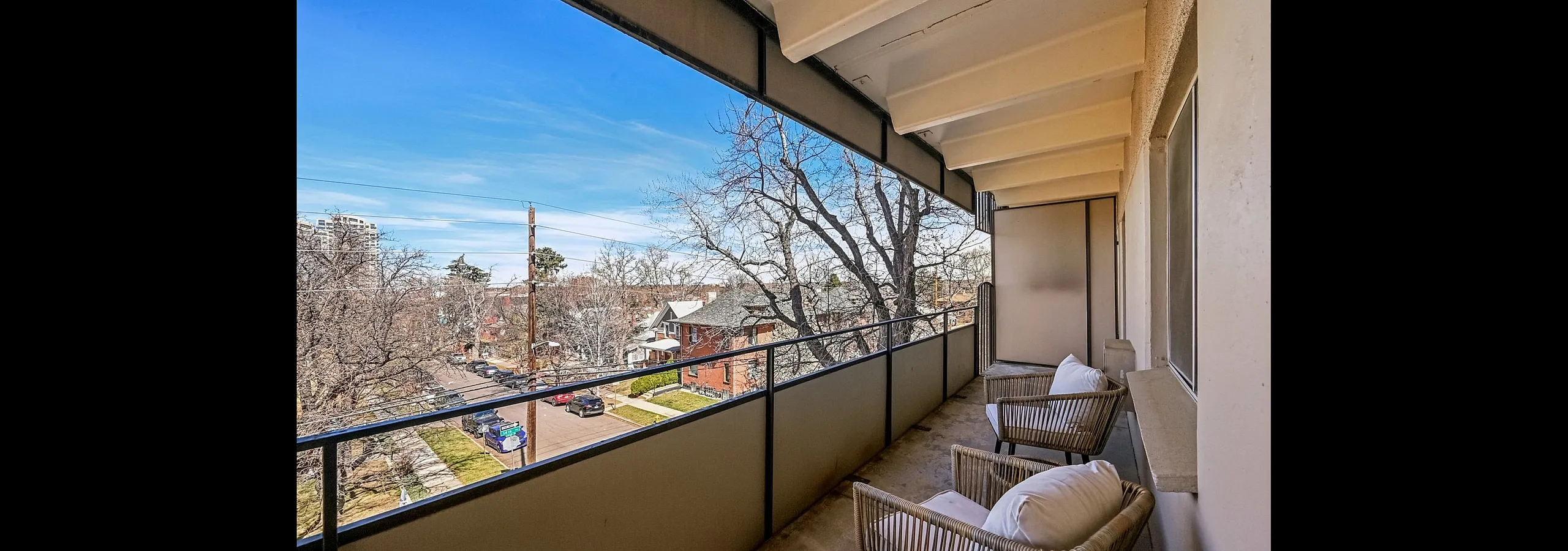 Charming balcony view with comfortable seating, overlooking a tree-lined street and classic neighborhood architecture.