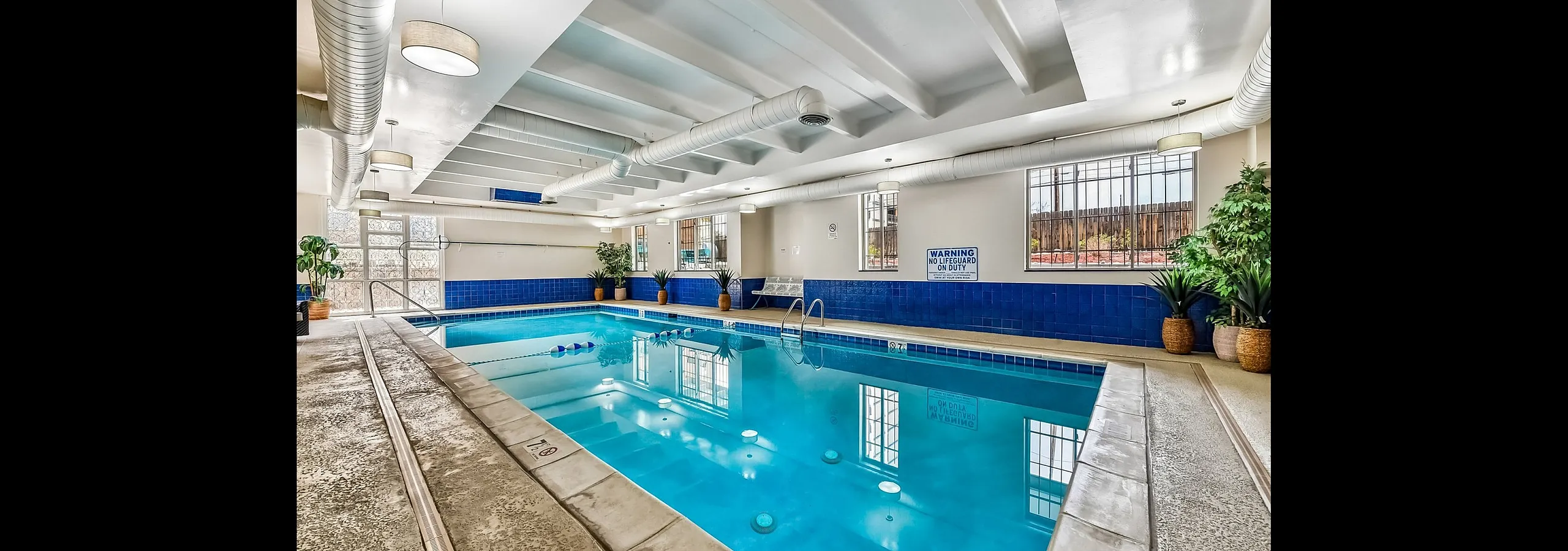 Inviting indoor swimming pool with stylish blue tiling, surrounded by elegant lighting and lush greenery.