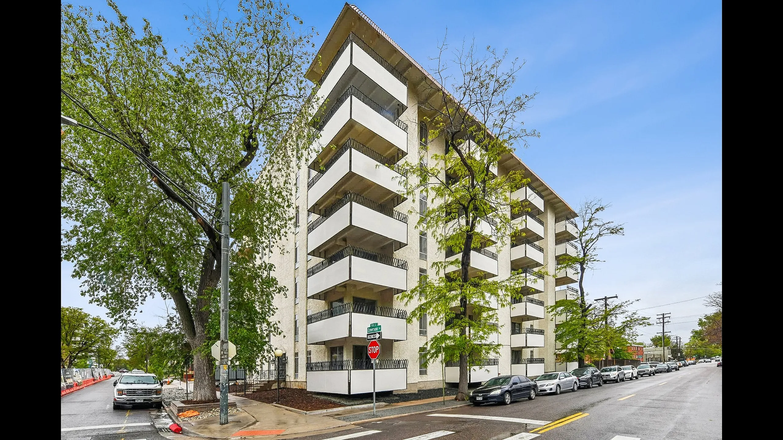 Charming residential building with modern balconies, nestled on a tree-lined street corner.