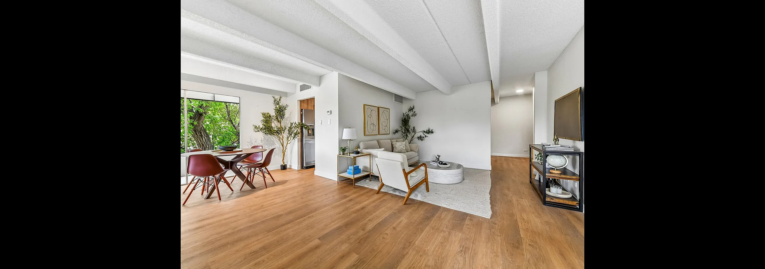 Bright and inviting open-concept living area featuring sleek hardwood floors, modern dining set, and cozy lounge space with stylish decor and natural light.