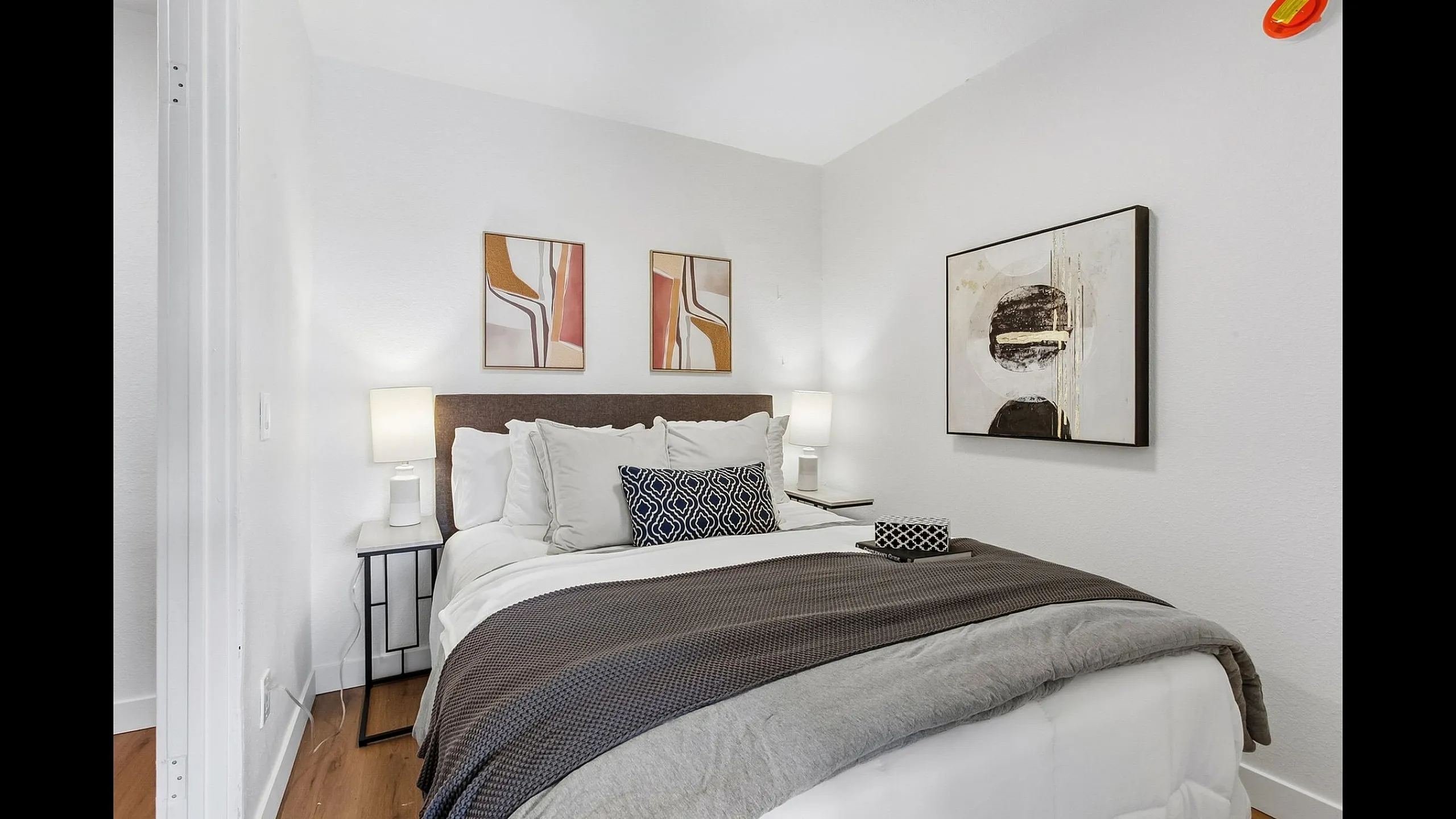 Inviting bedroom with modern decor, featuring cozy bedding, abstract wall art, and soft lighting for a serene atmosphere.