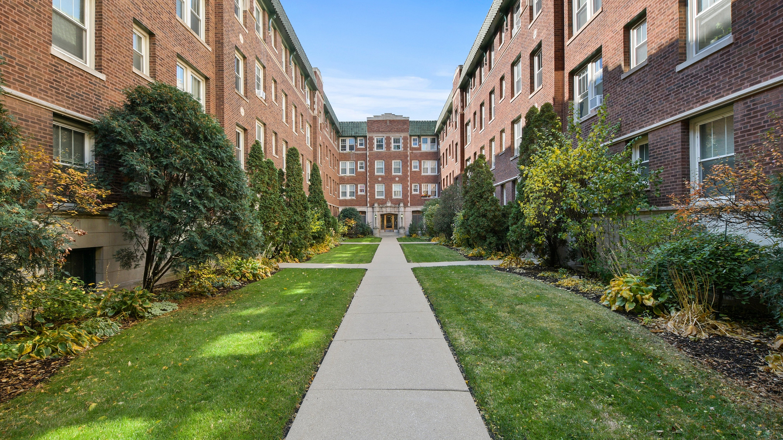 Charming brick apartment complex with lush green landscaping and a welcoming pathway.