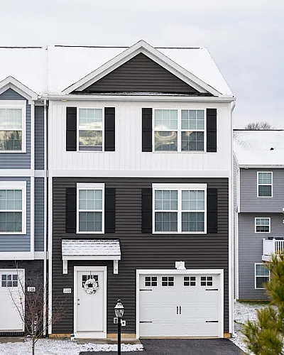 Charming townhouse with dark and light contrasting exterior, featuring snow-dusted roof and decorative wreath.