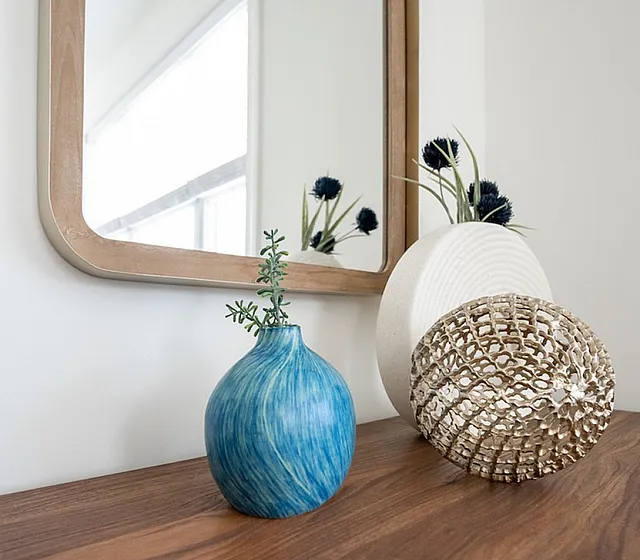 Elegant decor arrangement with a blue vase, decorative ball, and modern mirror on a wooden surface.