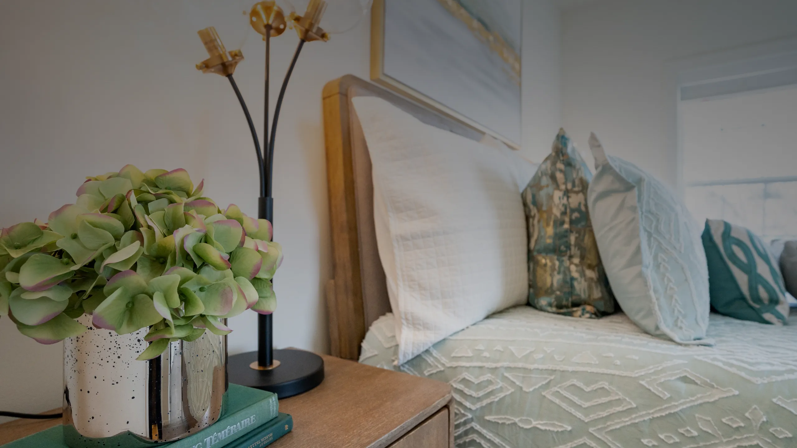 Inviting bedroom corner with elegant plush pillows, a modern table lamp, and vibrant green potted plant for a serene atmosphere.