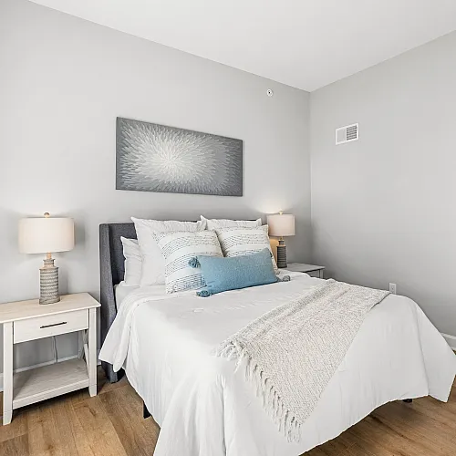 Chic bedroom with modern decor, featuring a cozy bed with plush pillows, elegant art piece, and warm wooden flooring.