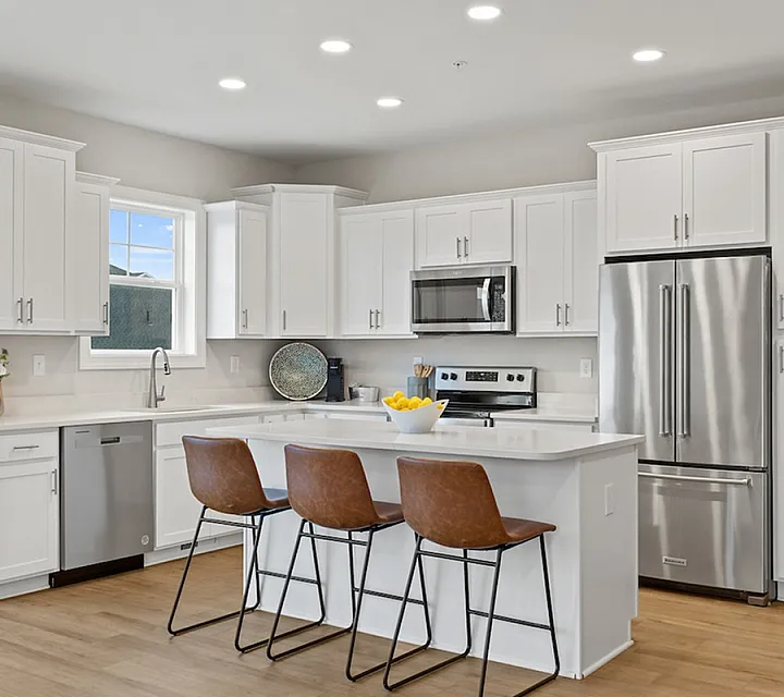 Modern kitchen with sleek white cabinets, stainless steel appliances, and a stylish island with brown leather bar stools.