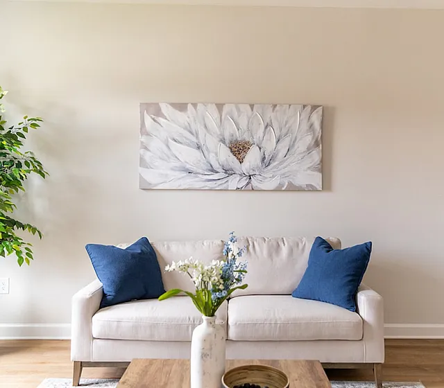 Bright and inviting living room with elegant white sofa adorned with blue cushions, vibrant green plant, and modern floral artwork.