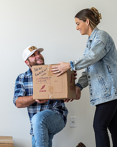 Joyful new homeowners unpacking boxes in a modern apartment with sleek wooden floors, creating a vibrant and inviting living space.